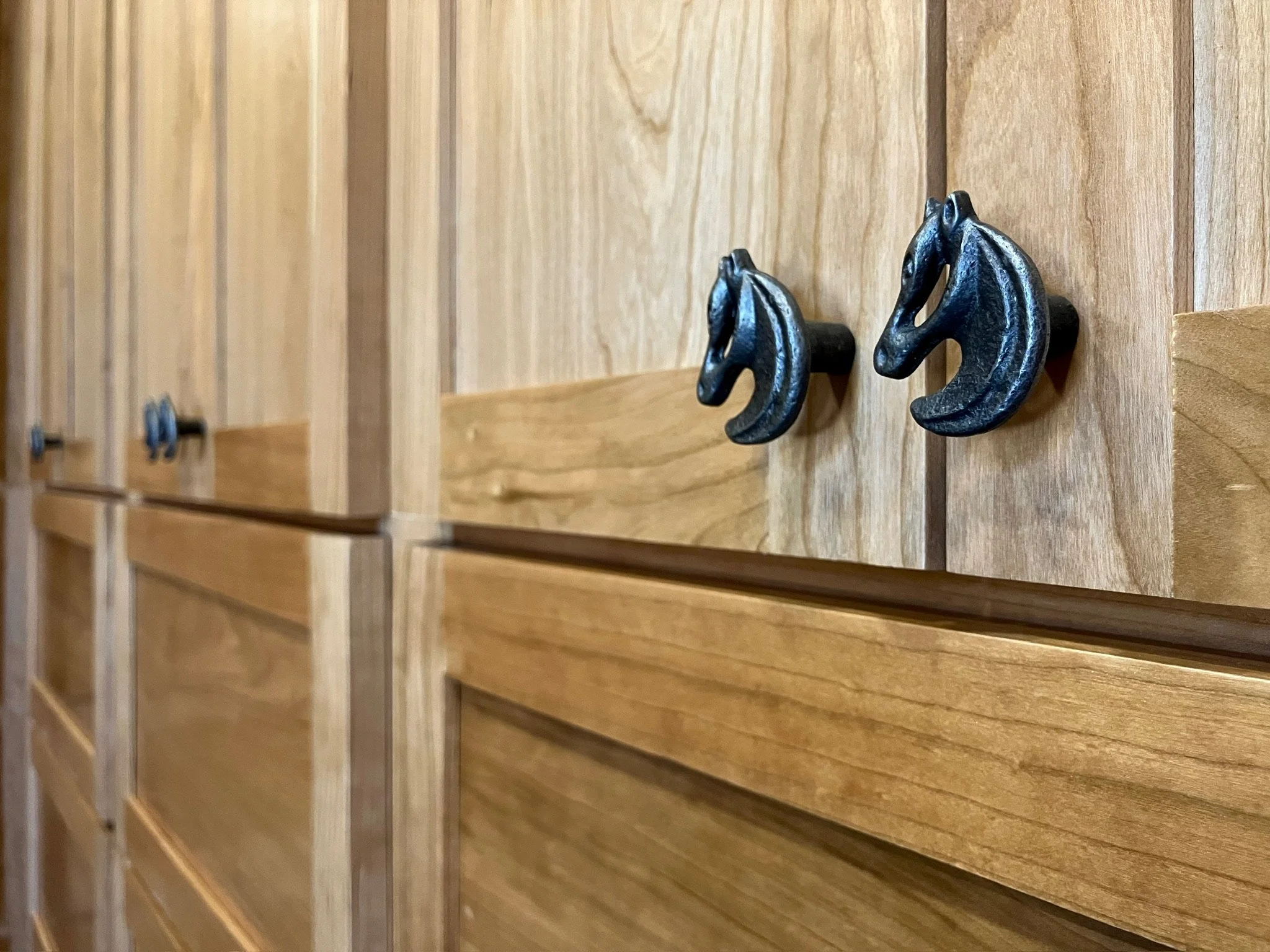 Close-up of a wooden cabinet with two black horse head-shaped handles.