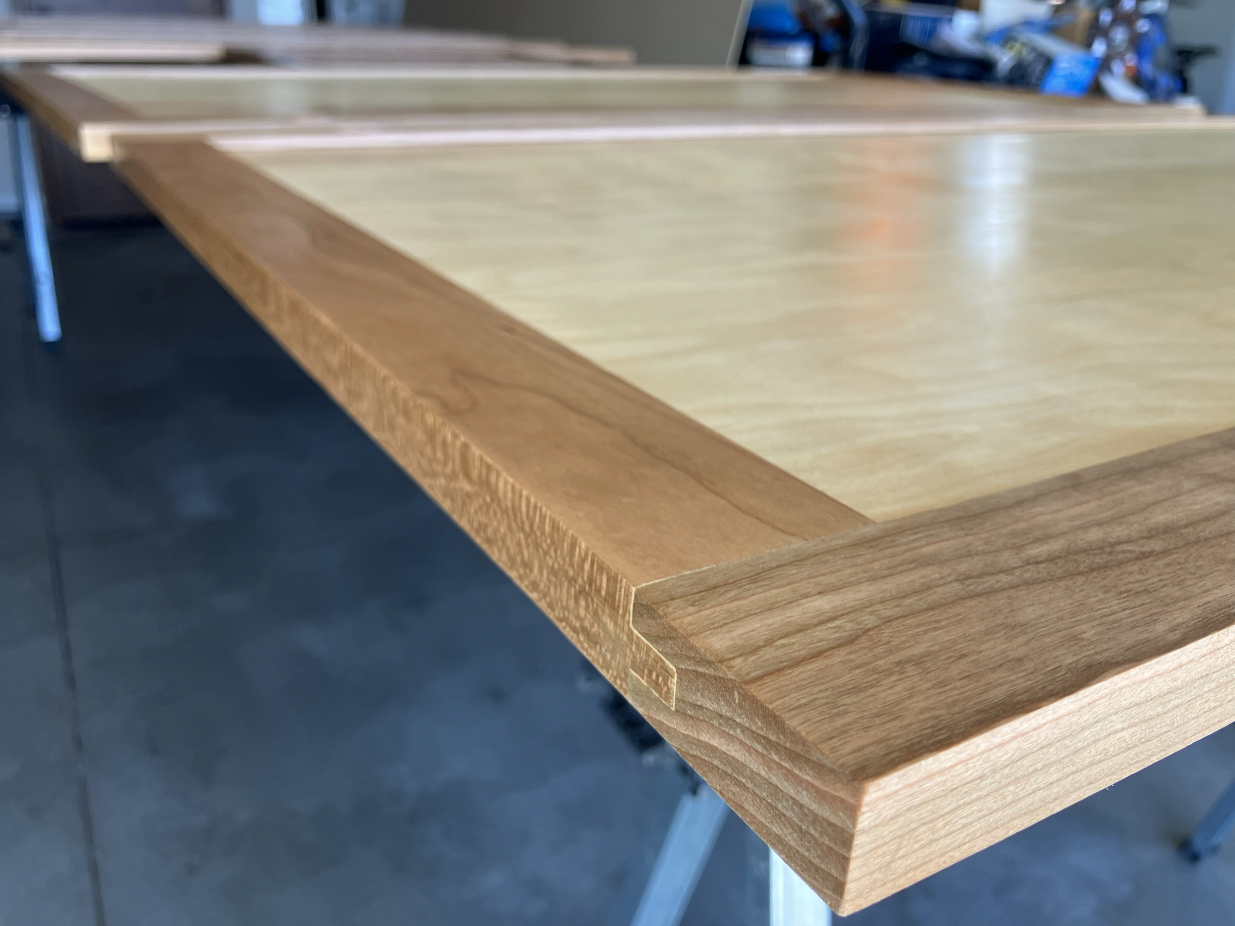 Close-up of a wooden table with a light-colored surface and a darker wood border, in an indoor setting.