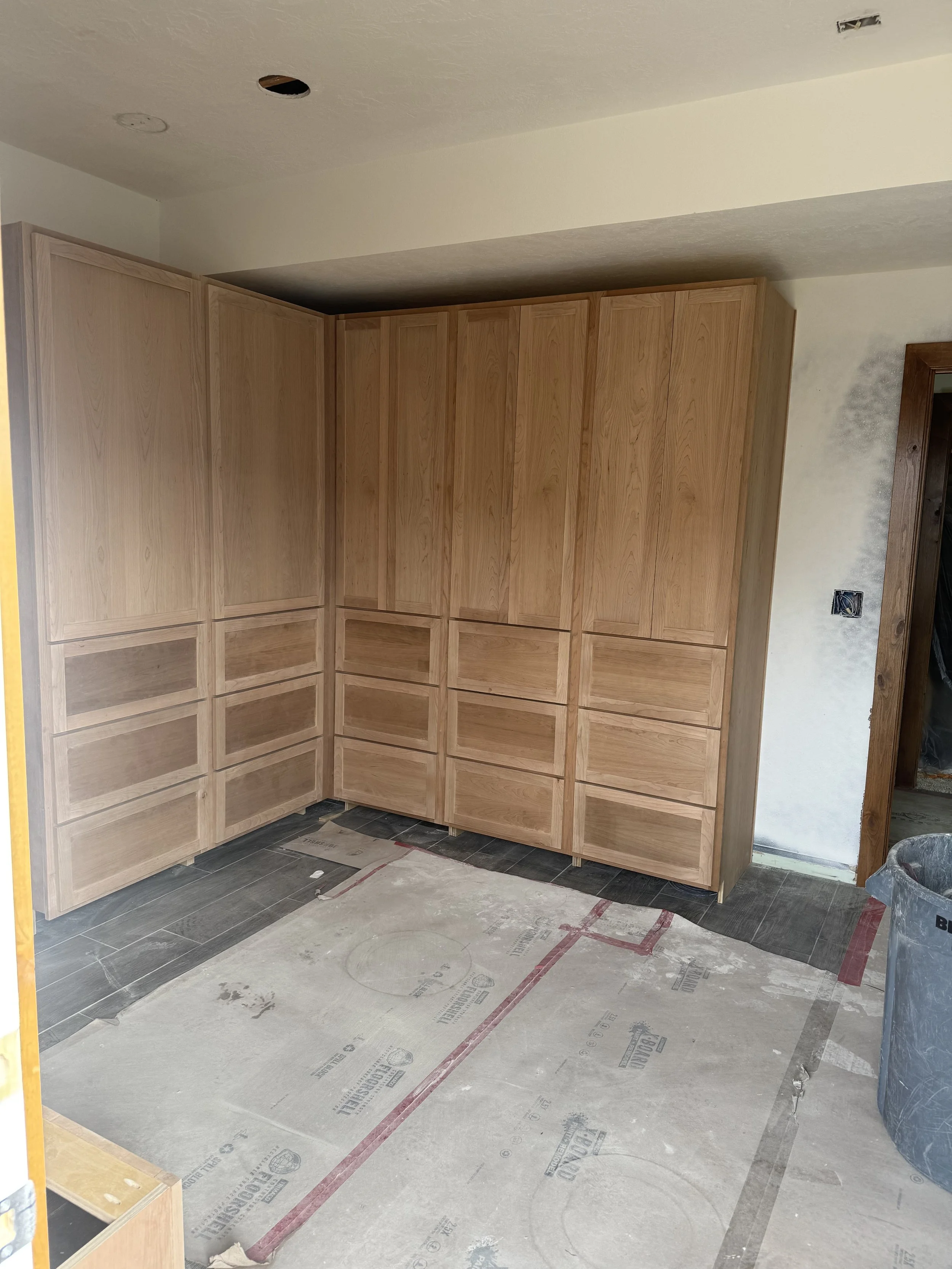 unfinished kitchen with wooden cabinets installed in the corner, gray tiled flooring, and a construction paper on the floor. An open doorway is visible on the right.