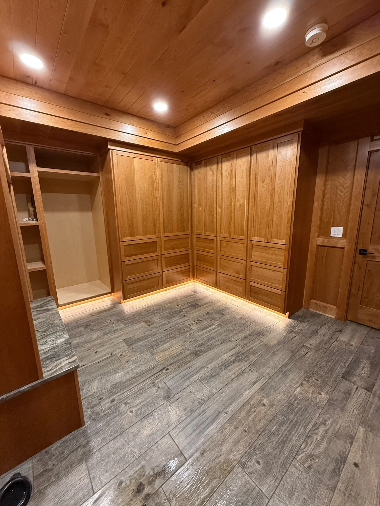 Empty walk-in closet with wood paneled walls and ceiling, gray tiled flooring, built-in shelves, and a closed door.