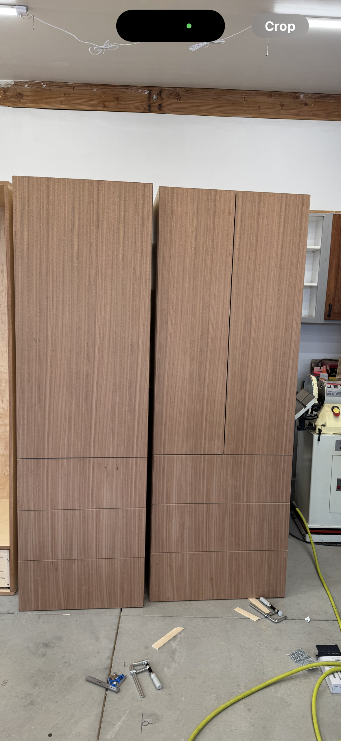 Two tall wooden cabinets or wardrobe units in a workshop, with construction tools and materials on the floor.