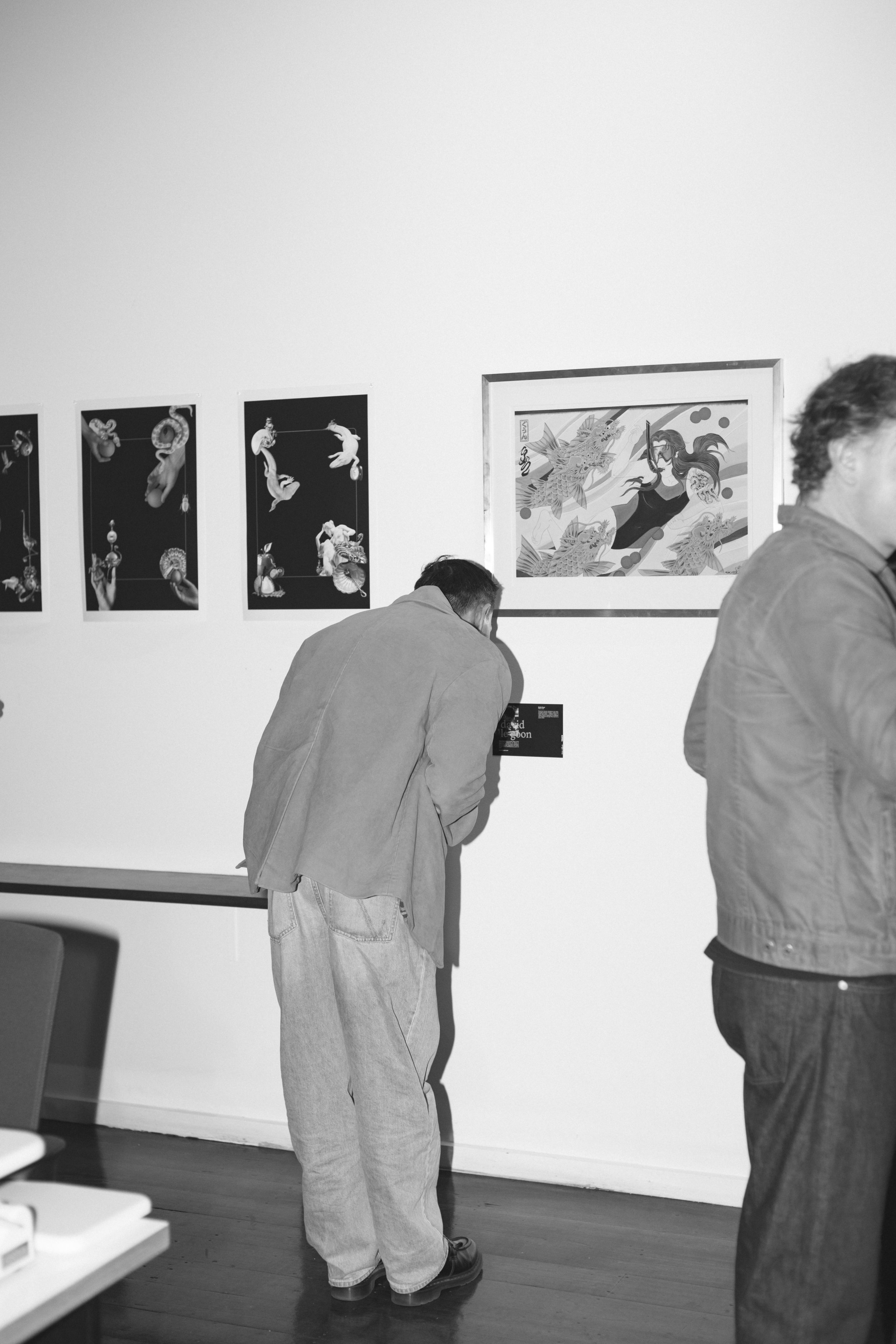 People observing artwork in an art gallery, with framed art pieces on the wall and individuals focused on the exhibition.