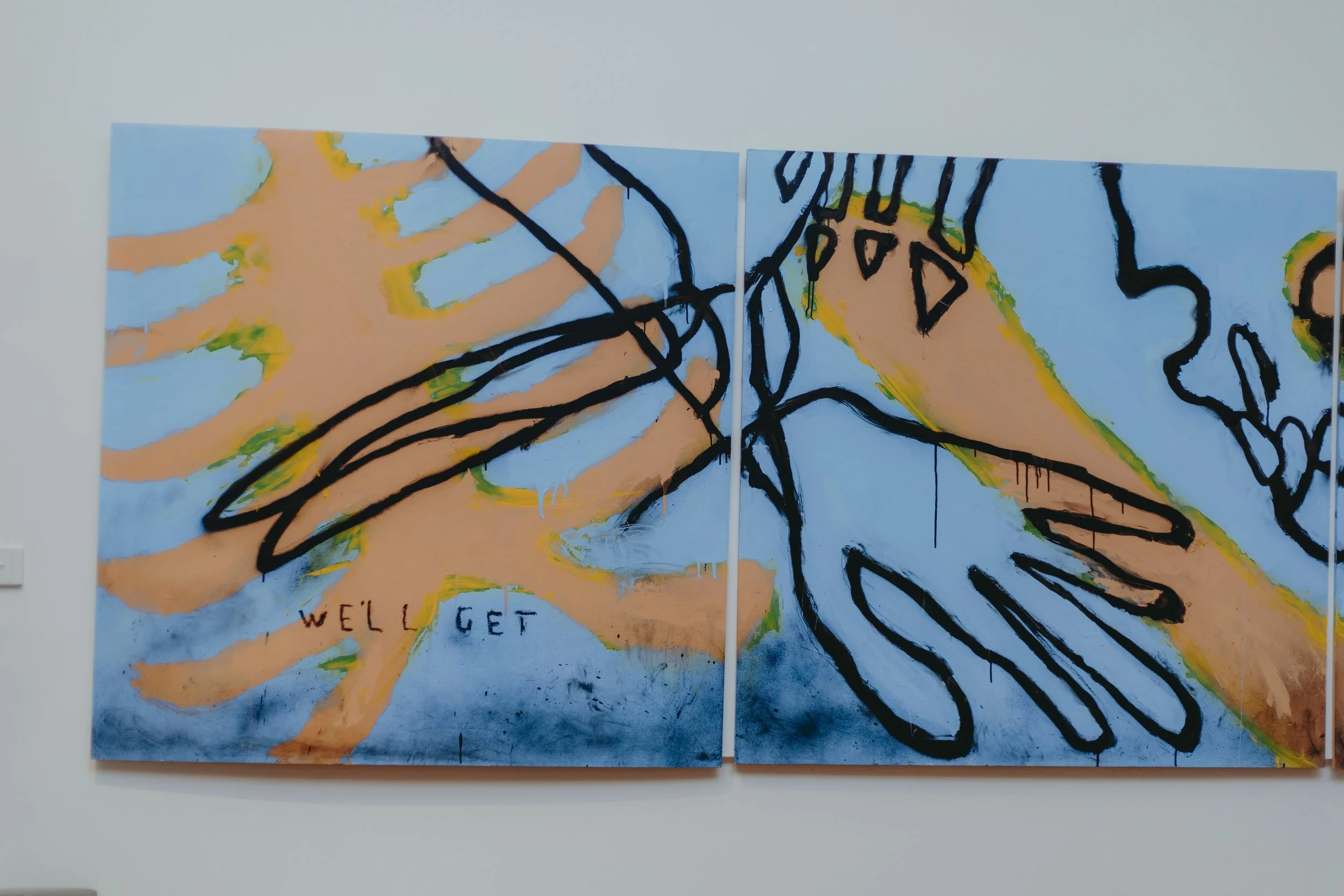 Abstract artwork on two canvases featuring handprints, black lines, and colorful accents. The phrase 'Well, I get' is written on the bottom left of the left canvas.