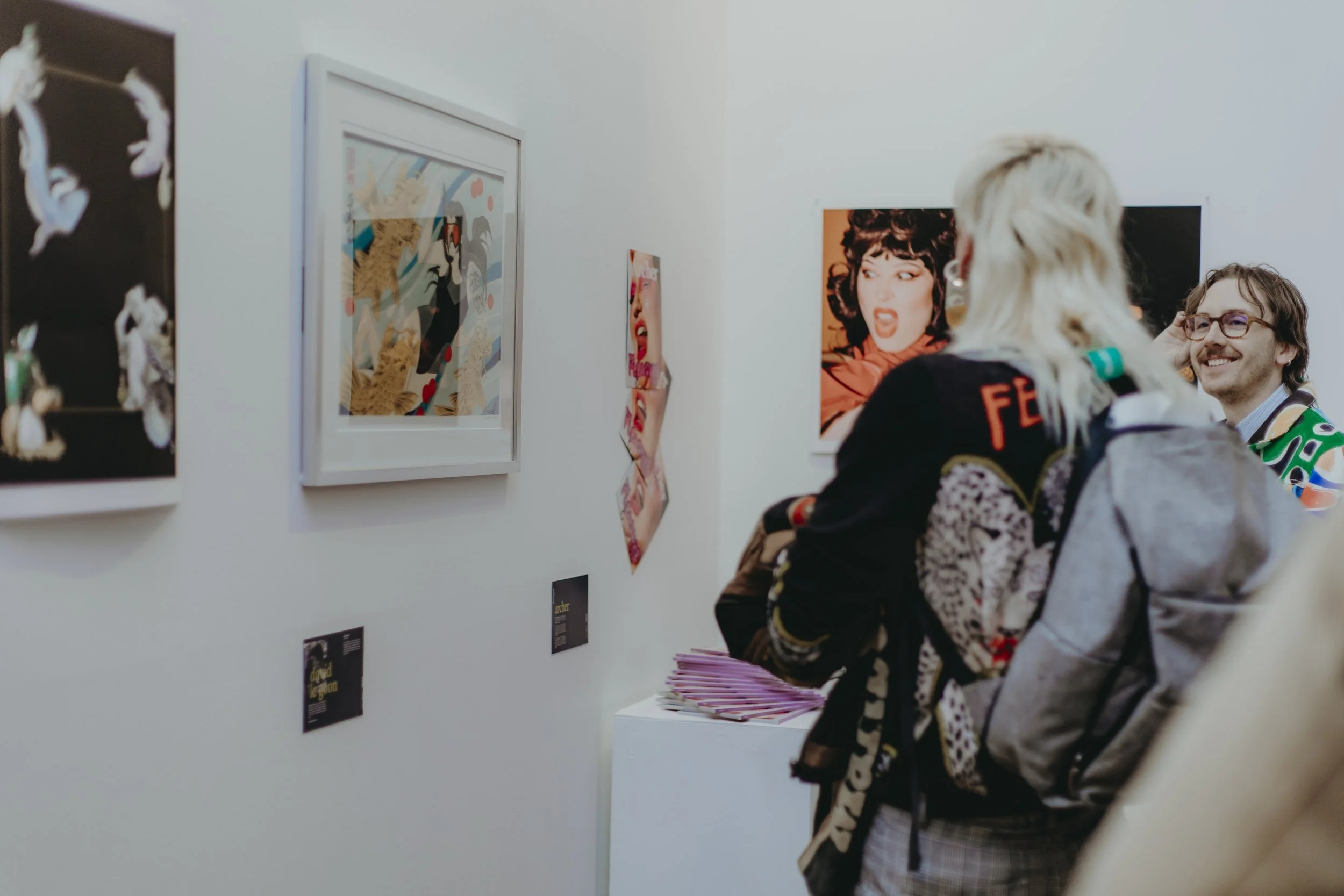 People viewing artwork and posters on the white gallery wall at an art exhibition.