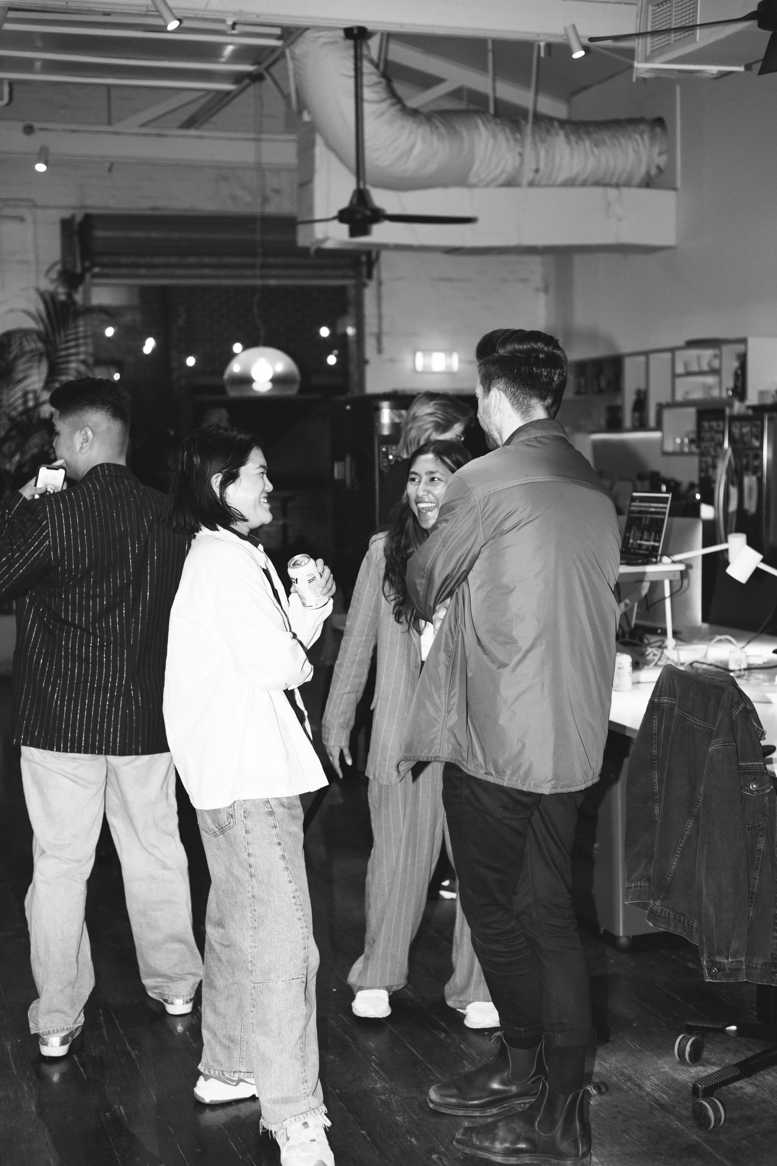 A group of people socializing in a modern indoor space with a casual atmosphere, engaging in conversation and smiling.