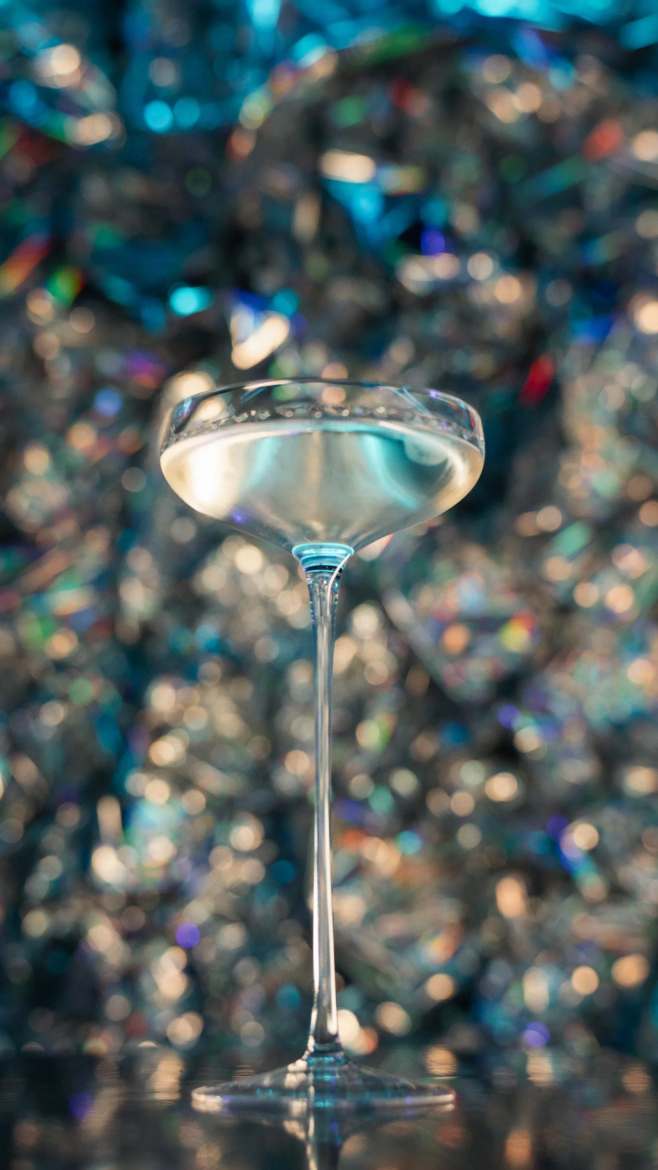 A cocktail glass with a clear liquid, set against a colorful, bokeh background.