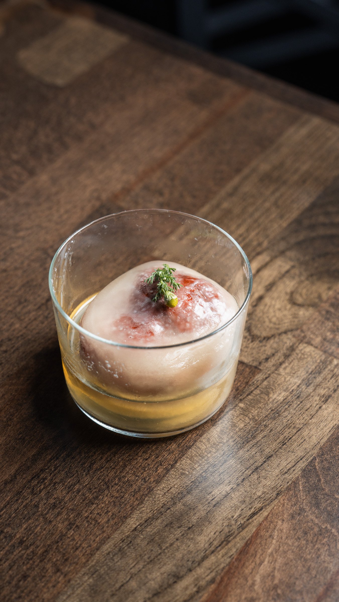 A glass with a dessert topped with a small green garnish, possibly a sprig of thyme, on a wooden table.