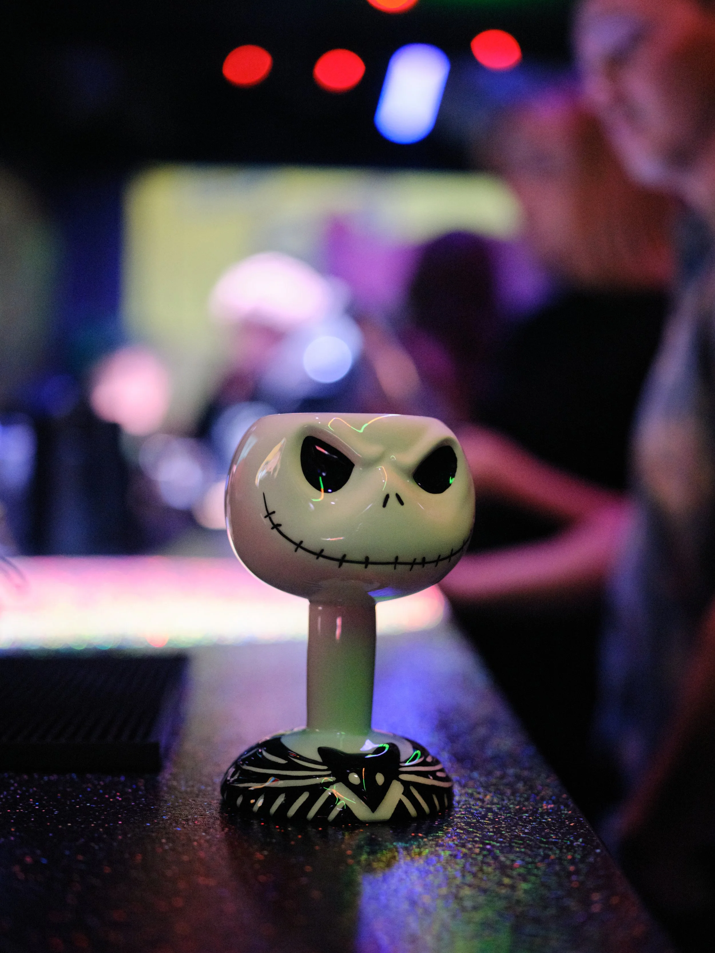 A skull-shaped decorative object placed on a table, with colorful lights and blurred background, creating a vibrant atmosphere.