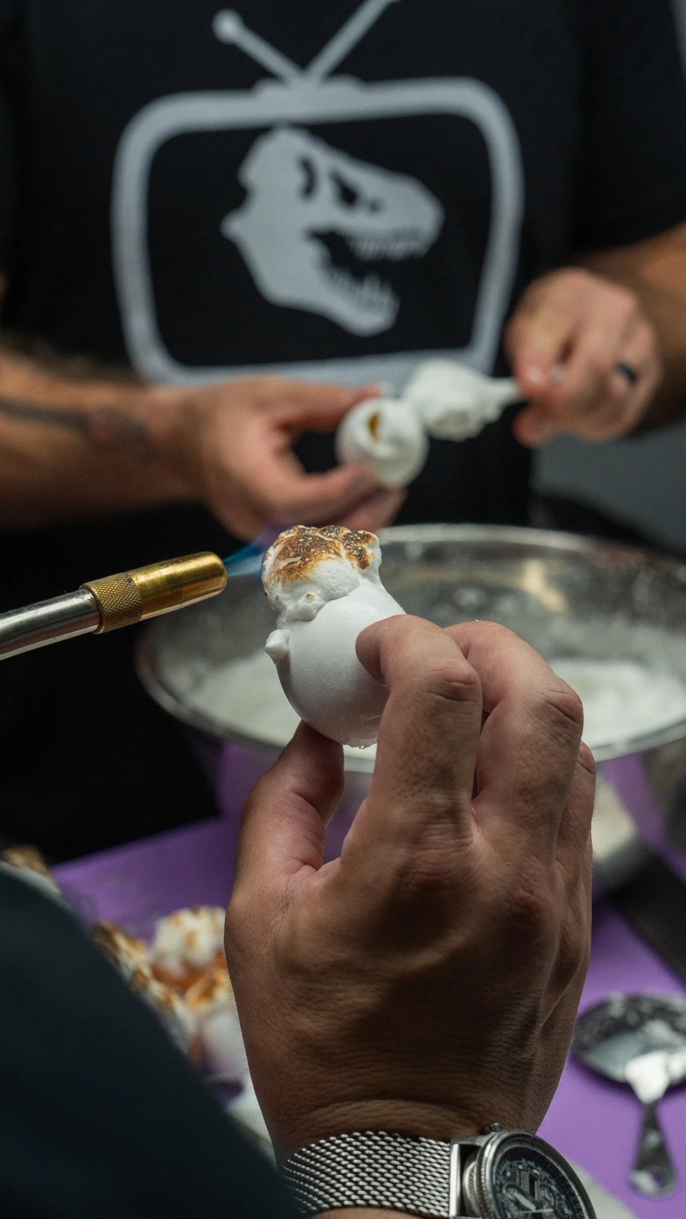 Person preparing toasted meringue treats, with a torch, in a kitchen or food prep area.