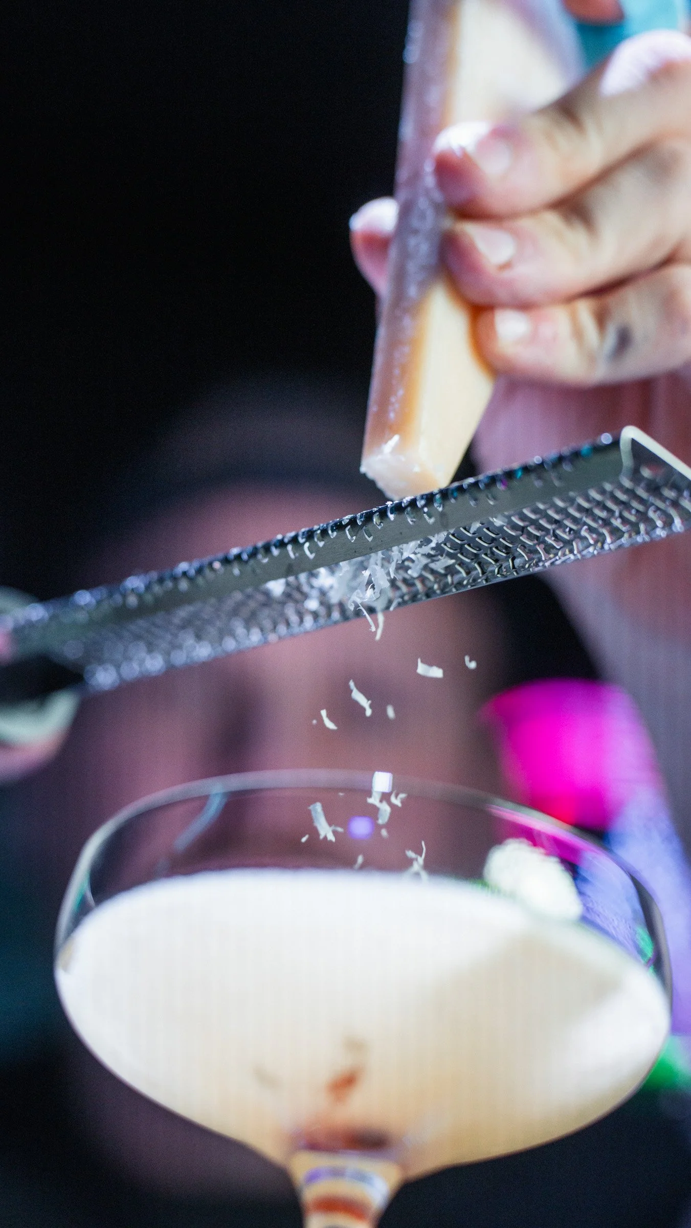 A person grating cheese over a cocktail glass filled with a white beverage.
