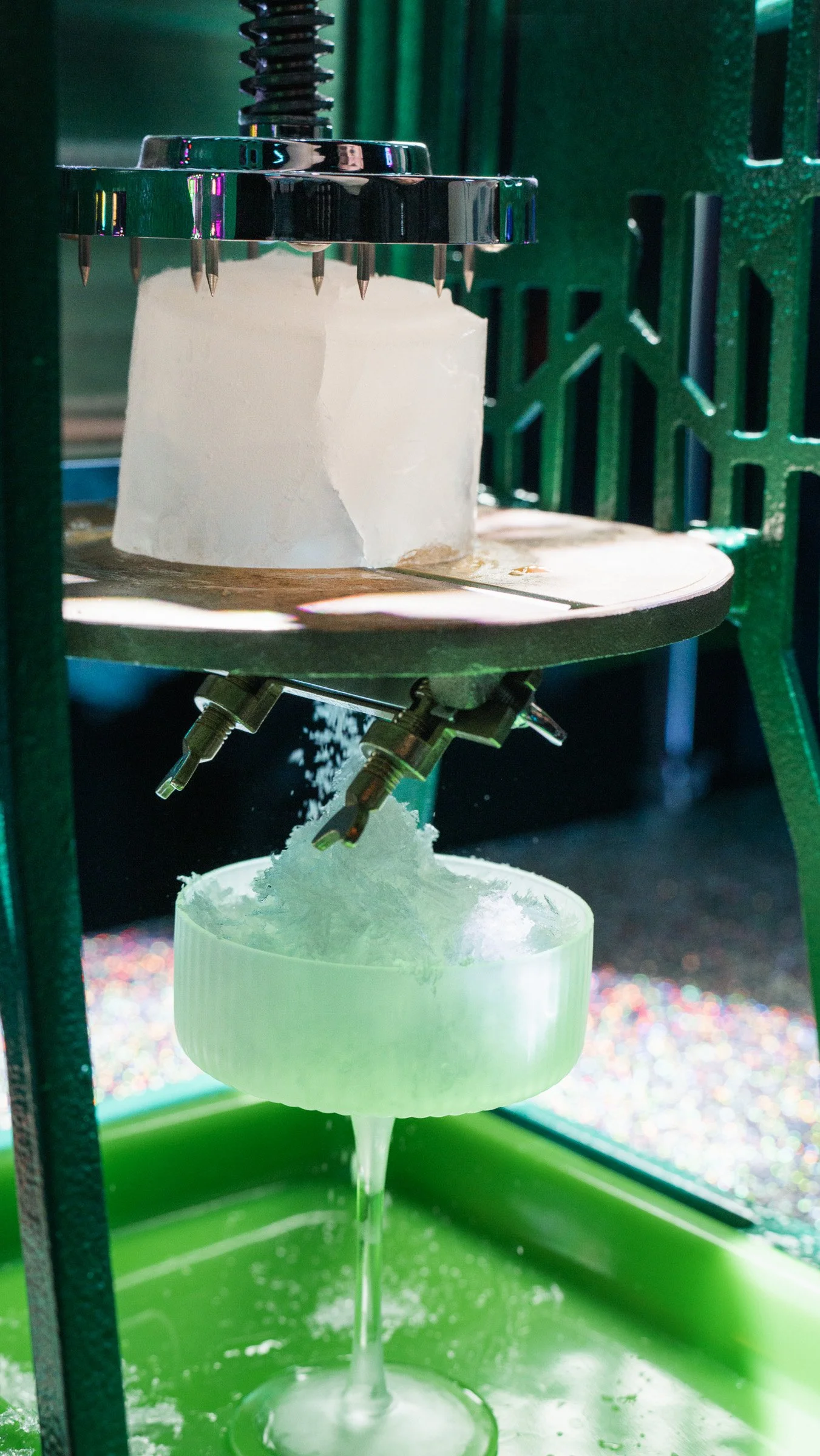 A cotton candy machine with a large cone of pink cotton candy spinning on top, and fluffy spun sugar falling into a white container below.