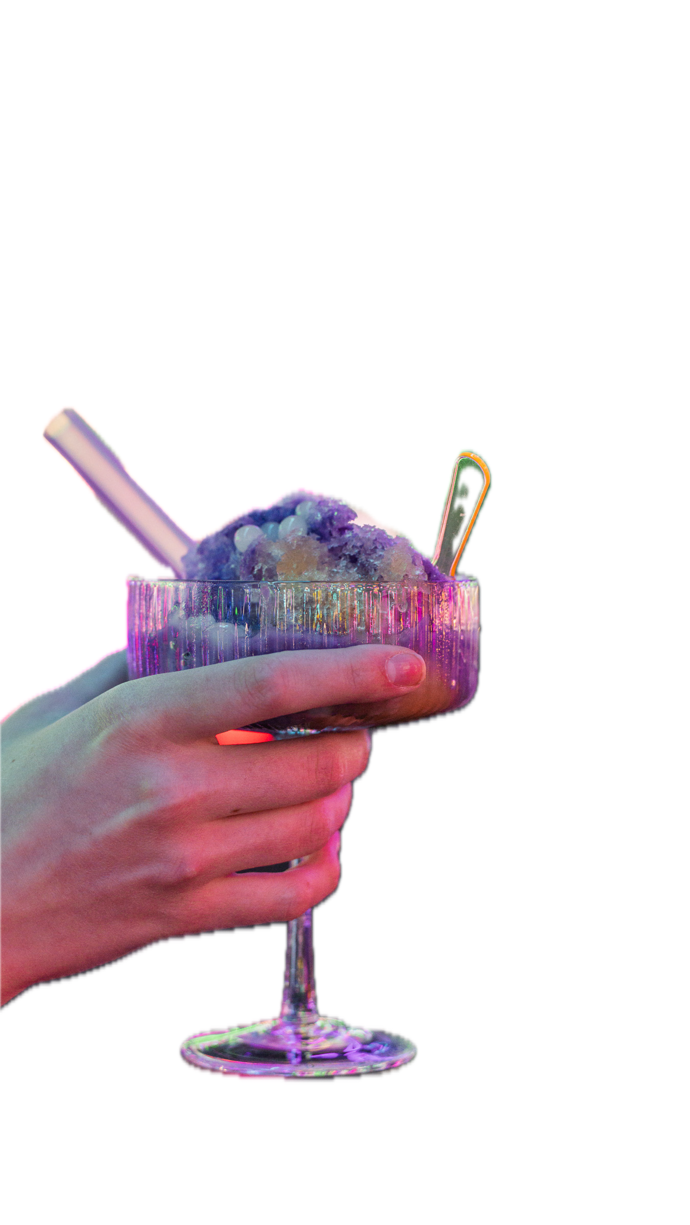 A person's hand holding a colorful glass bowl filled with ice cream, topped with small candies, and a spoon and straw inside.