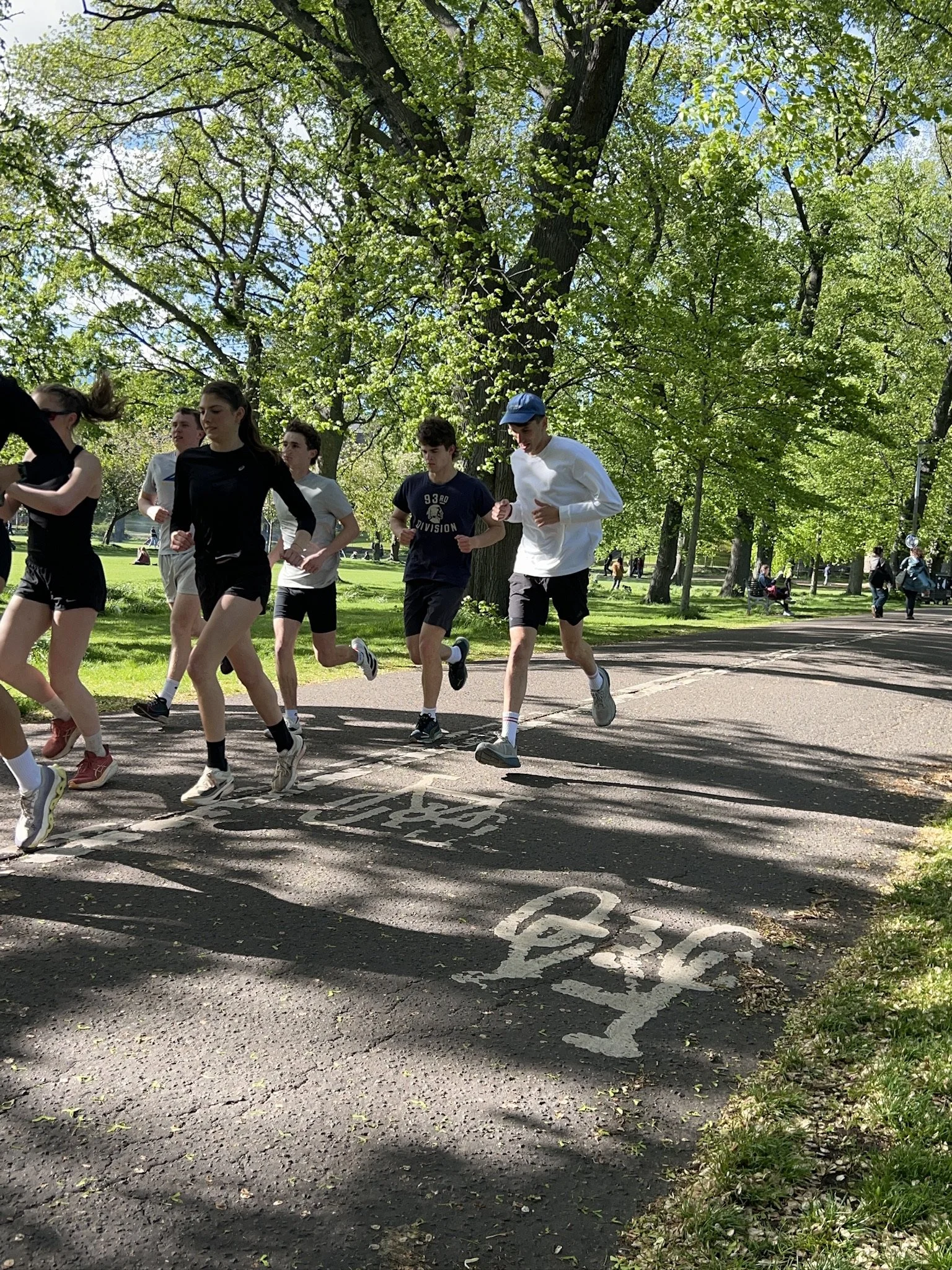 A group of young people running on a path in a park with green trees and blue sky overhead.