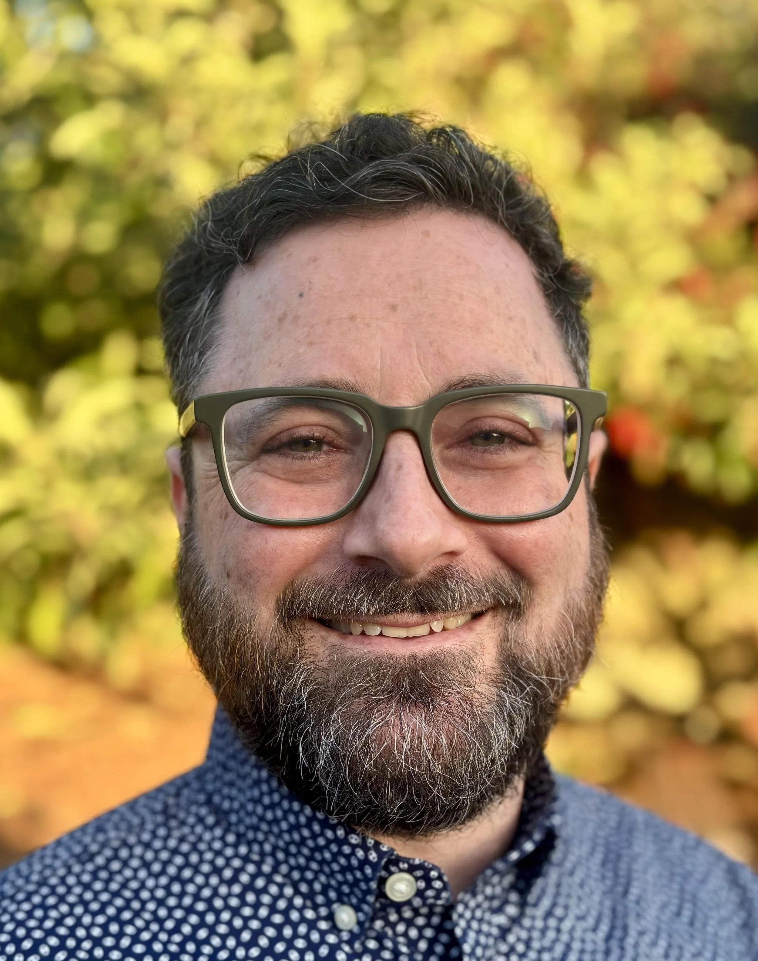 Man with green classes, beard and short hair smiling 
