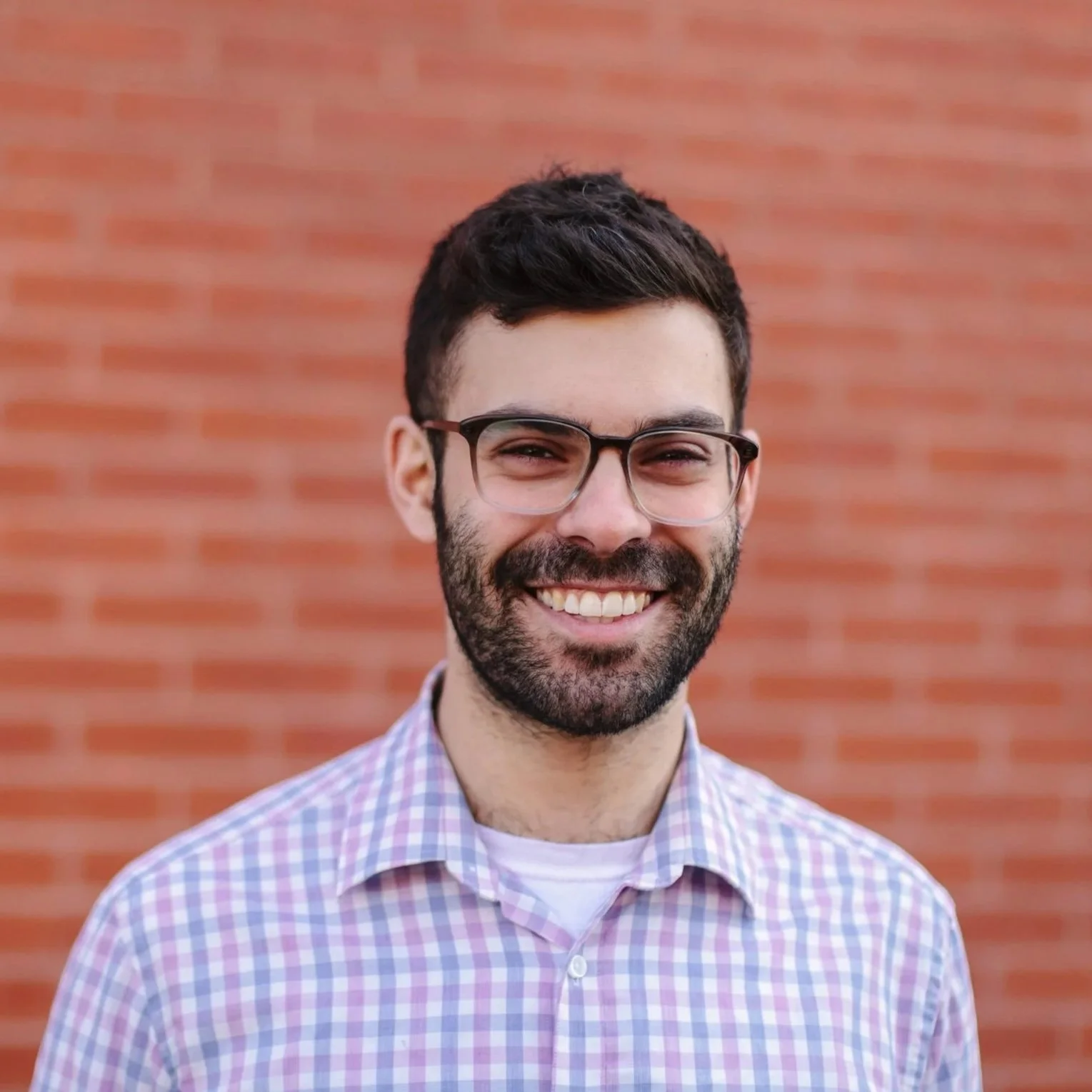 Black and white photo of woman with shoulder-length hair, collared dark shirt, smiling and posing at camera with hands in jean pockets