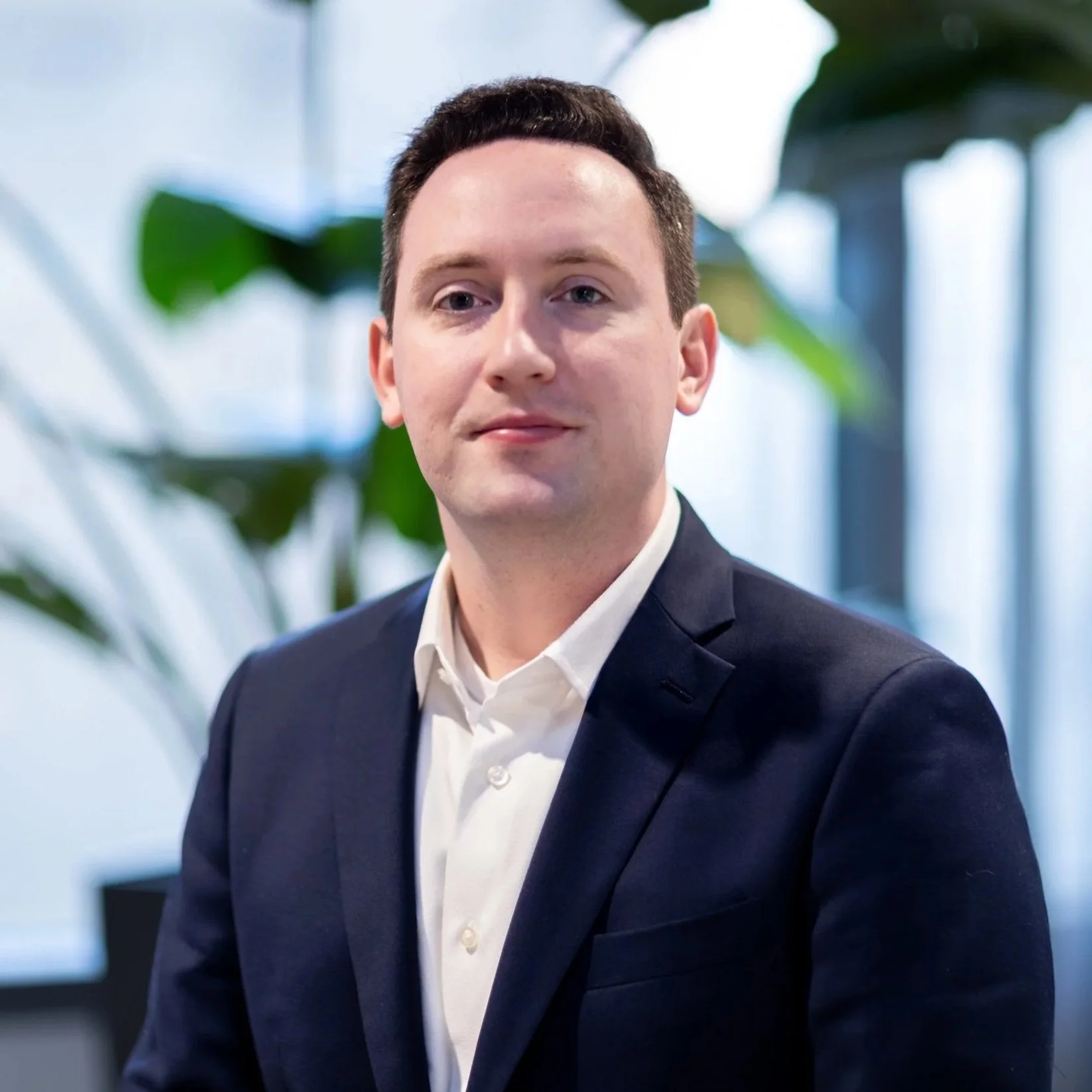 Man posing in blue suit and white collared shirt with short brown hair