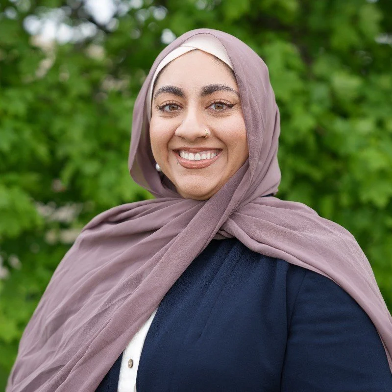 Woman posing with short brown hair and a teal necklace smiling