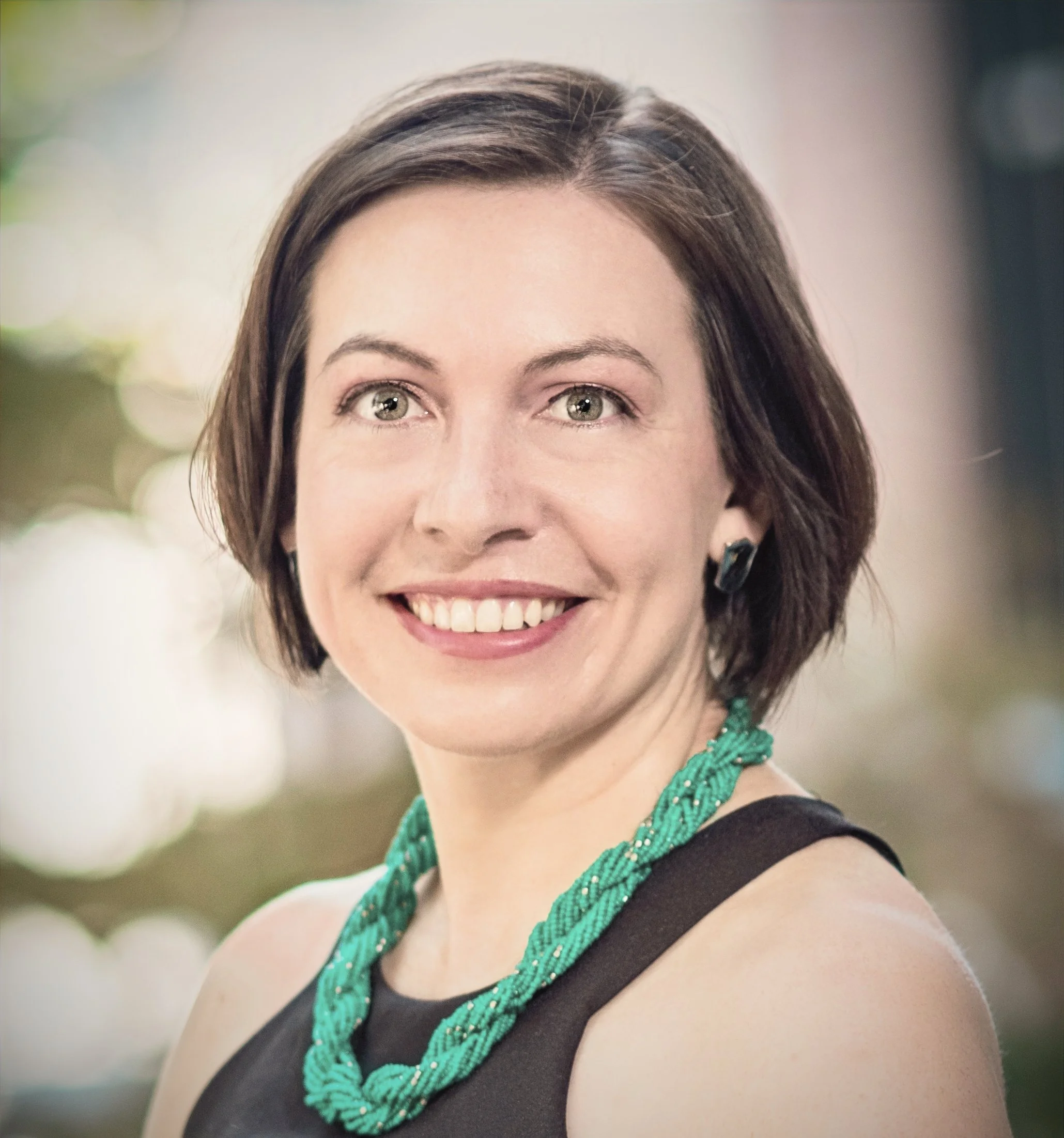 Woman posing with short brown hair, blue shirt with a light grey cardigan, and smiling
