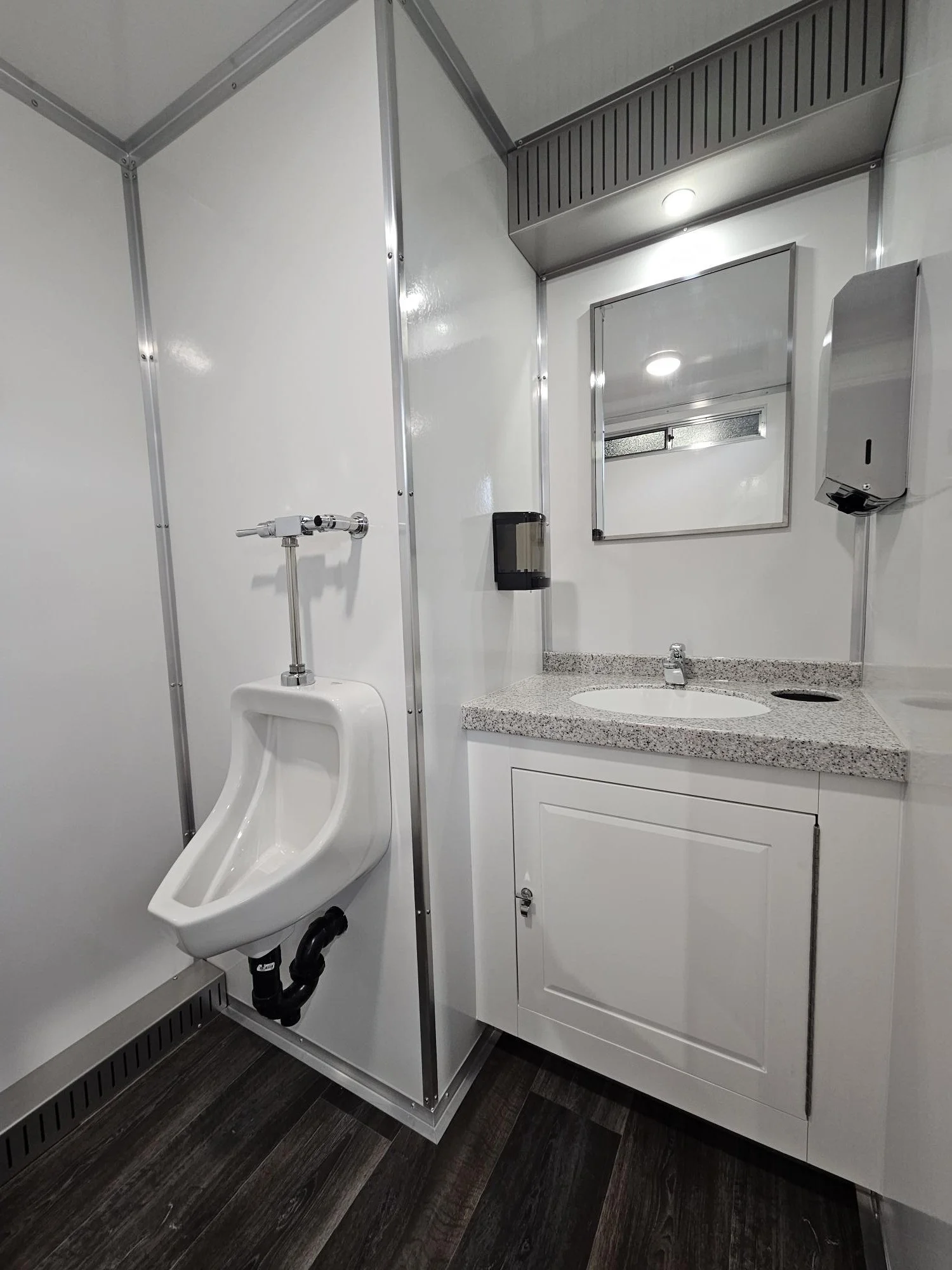 Rentable restrooms with a urinal on the left, a granite countertop with a sink, a mirror, a wall-mounted soap dispenser, a paper towel dispenser, and modern lighting fixtures.