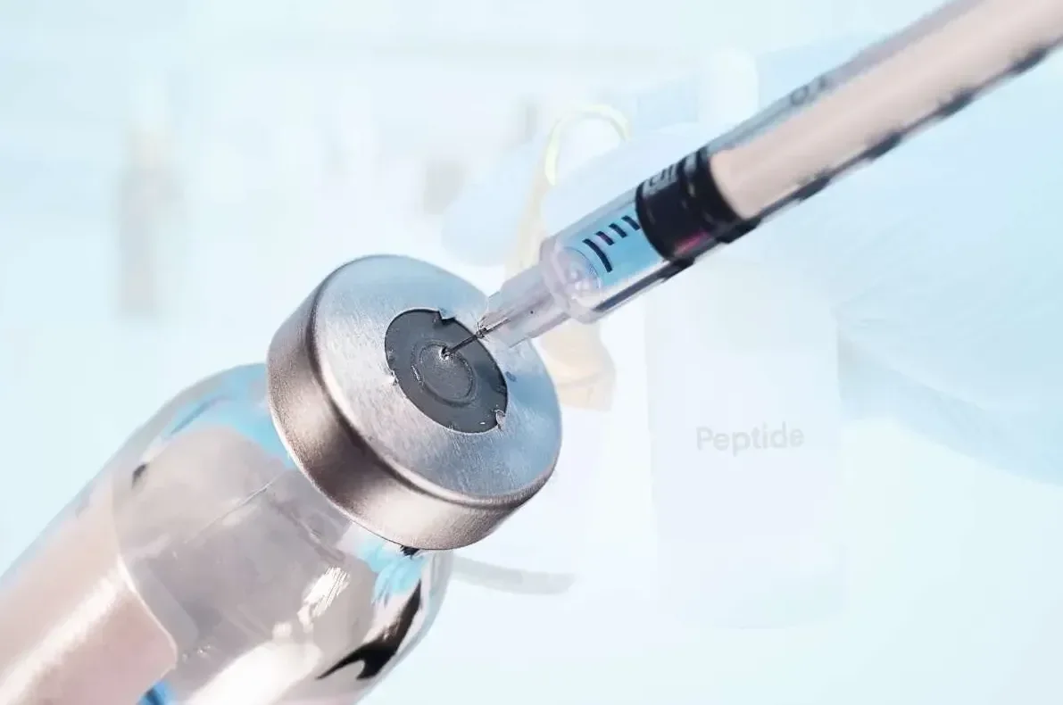 Close-up of a syringe injecting a clear liquid into a small vial on a light background.