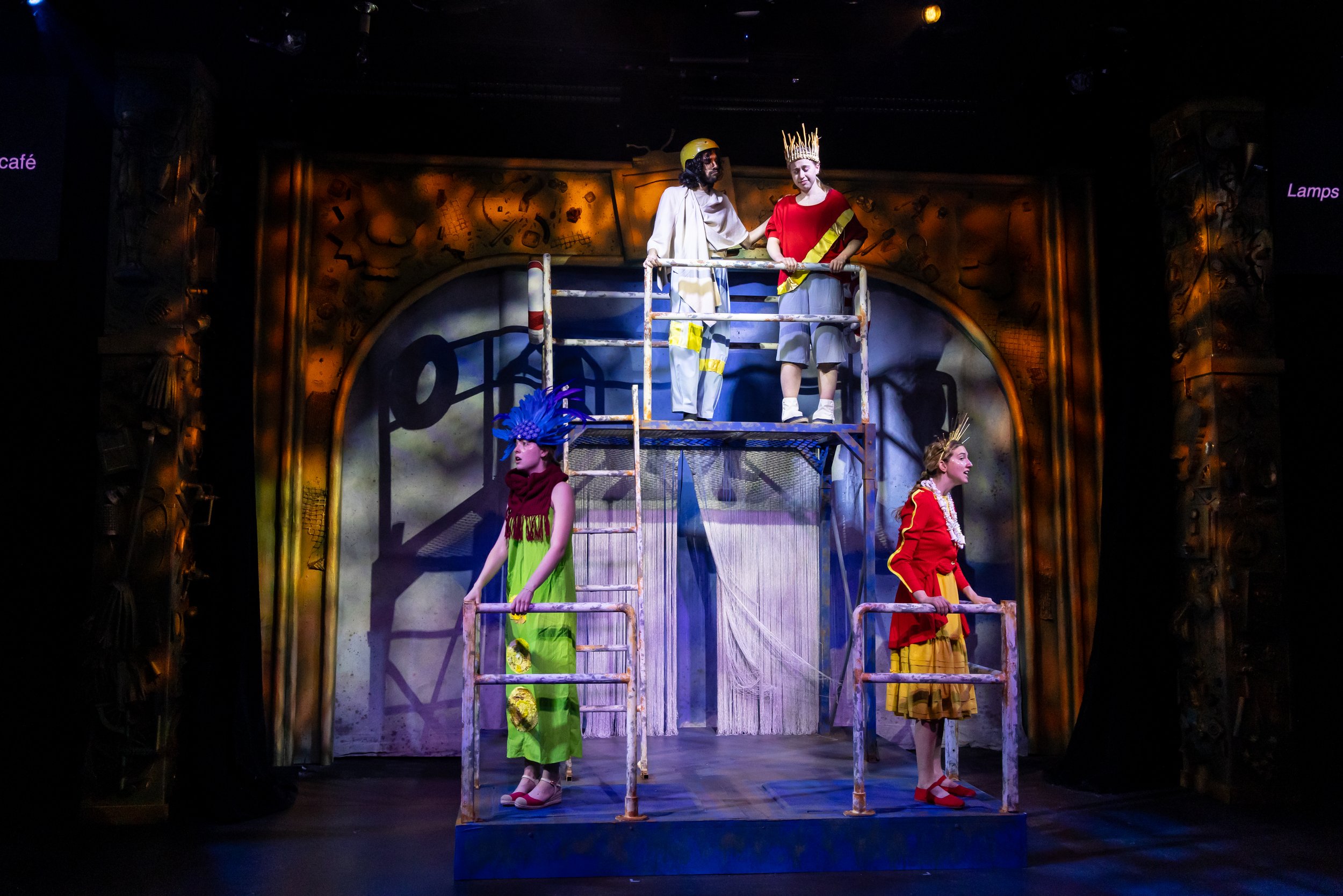 Theater stage with five actors in colorful costumes, standing on scaffolding, during a scene from a play.