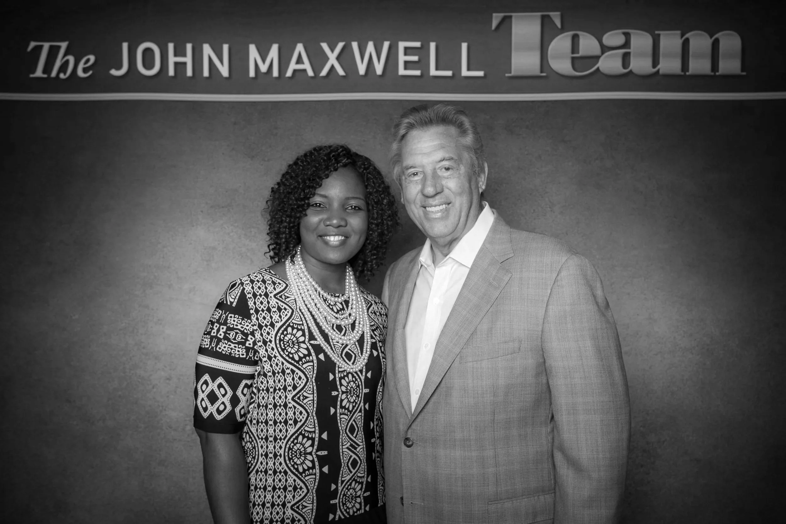 A woman with curly black hair and a professional dark blazer smiling while holding a microphone, with the text 'Executive Coaching' overlayed on the image of Dr Fofo Ilevbare with John Maxwell .