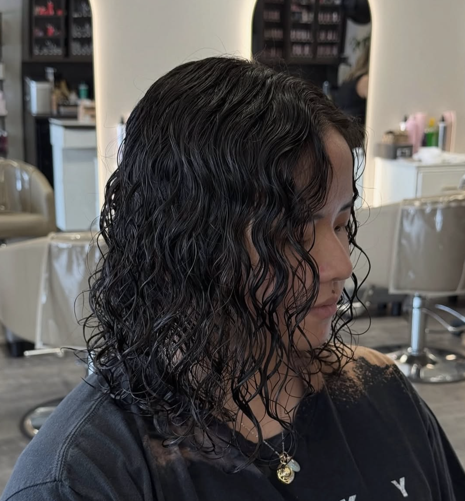 Woman with wet curly black hair sitting in a salon