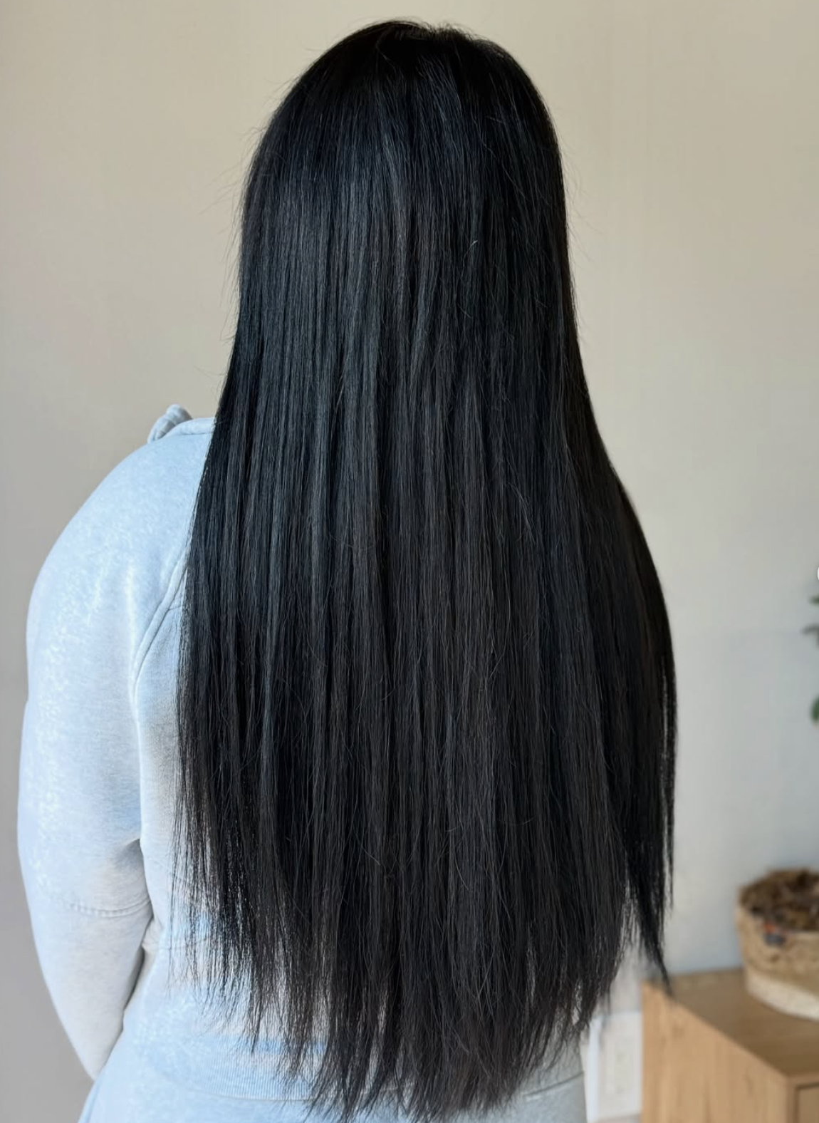 A woman with long, straight, black hair standing indoors against a neutral background.