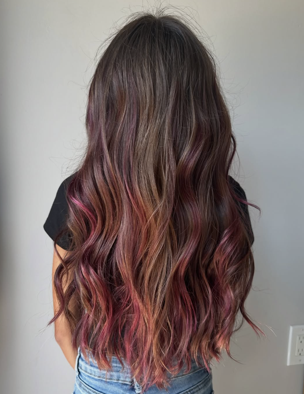 Long wavy brown hair with pink and purple highlights worn by a person in a black top and blue jeans.