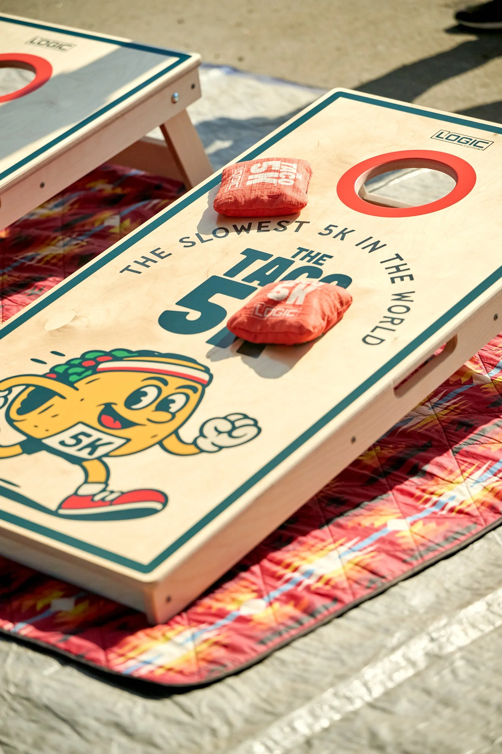 Cornhole game boards with bean bags on top, placed on a colorful quilted blanket outdoors.