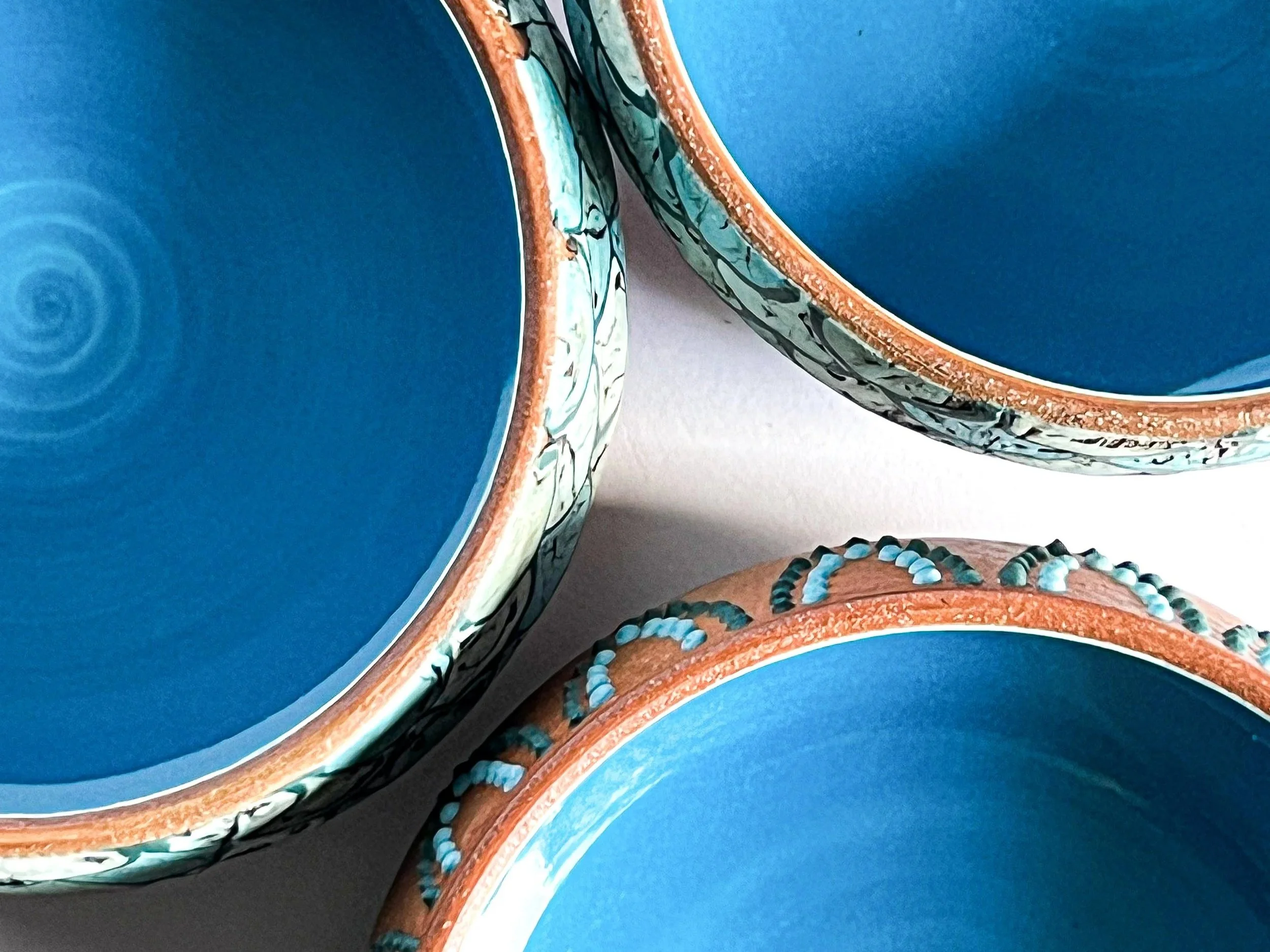 Close-up of three ceramic bowls with intricate exterior patterns, blue interiors, and a textured design along the rims.