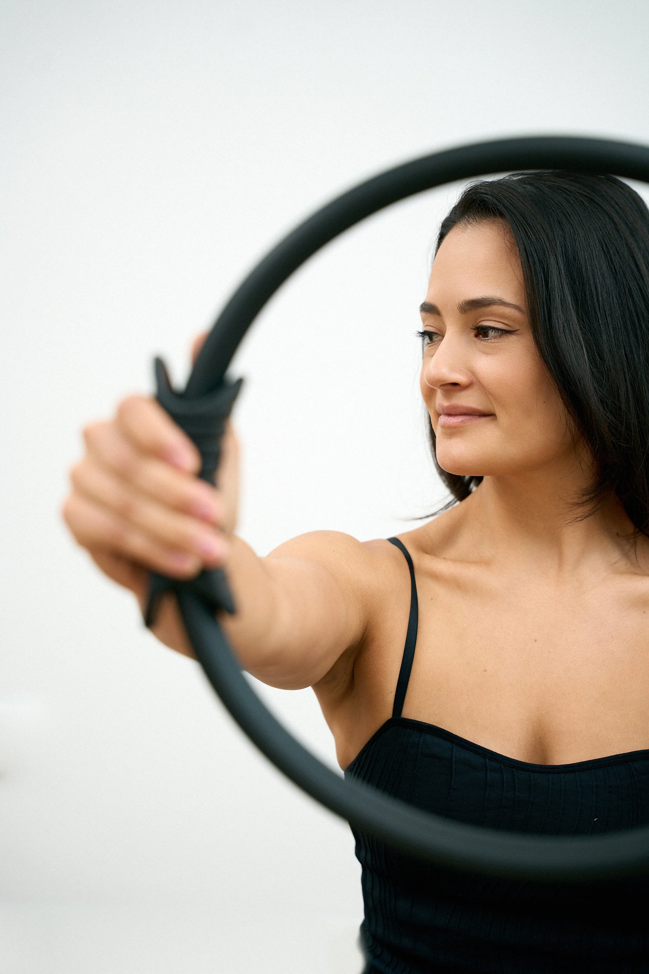 Eine junge Frau hebt ein schwarzes Fitness-Workout-Gerät und sieht es nachdenklich an.