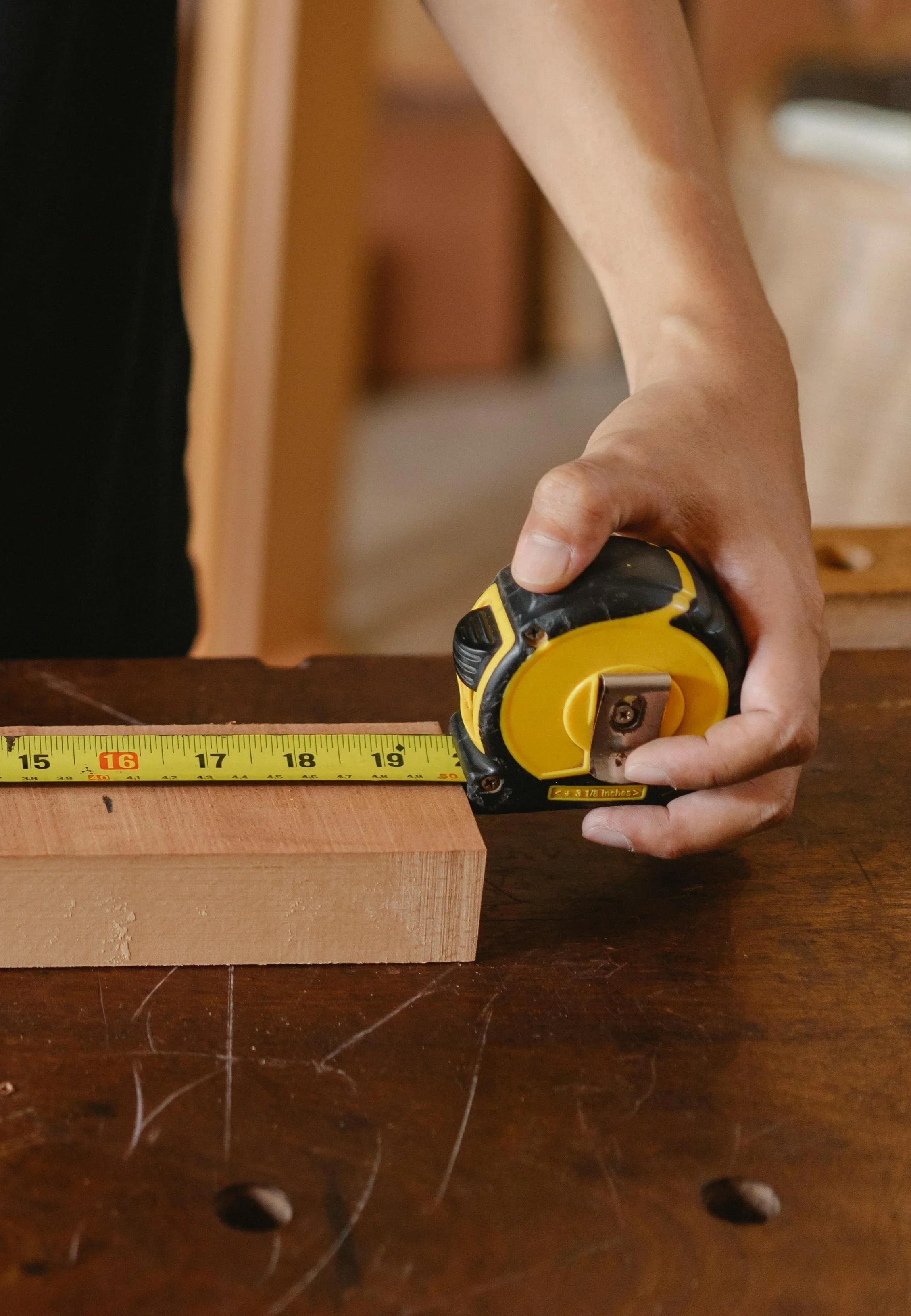 Person measuring a wood block with a tape measure on a wooden workbench.