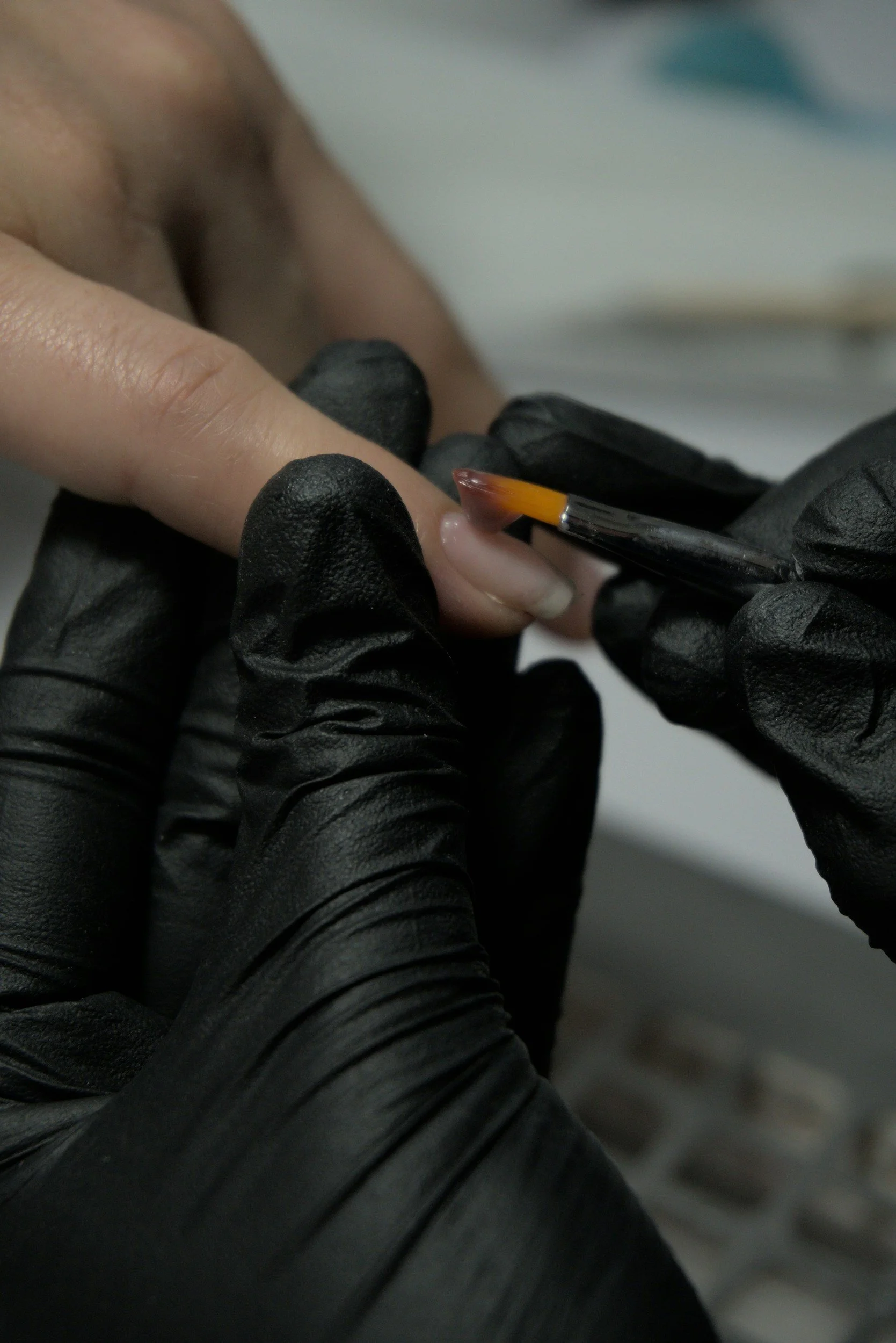 Close-up of a student technician applying precision hard gel using a brush technique during one-on-one nail training at Maison d'Or.