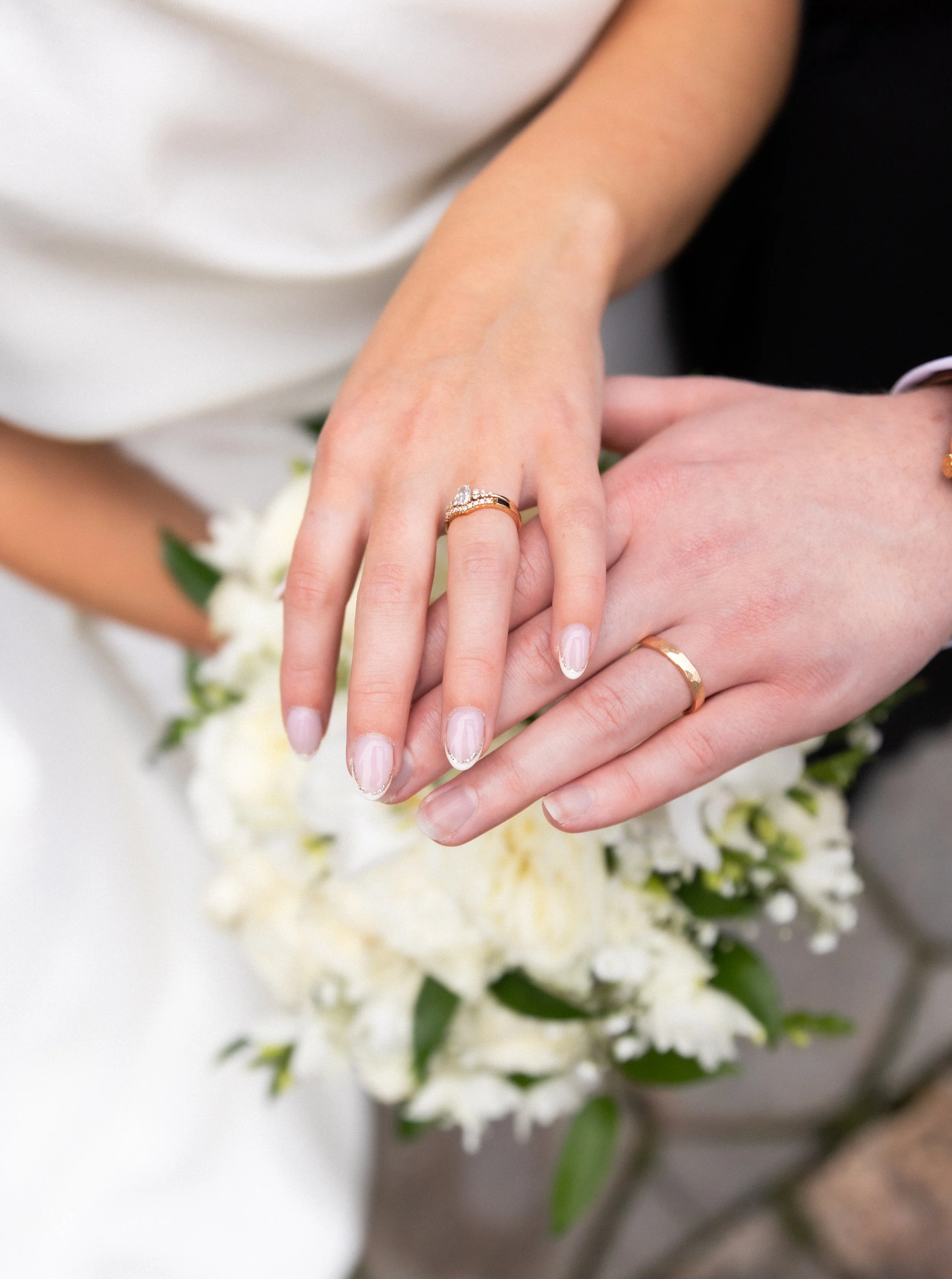 Hääparin kädet joissa näkyy sormukset ja kaunis kukkakimppu taustalla. 