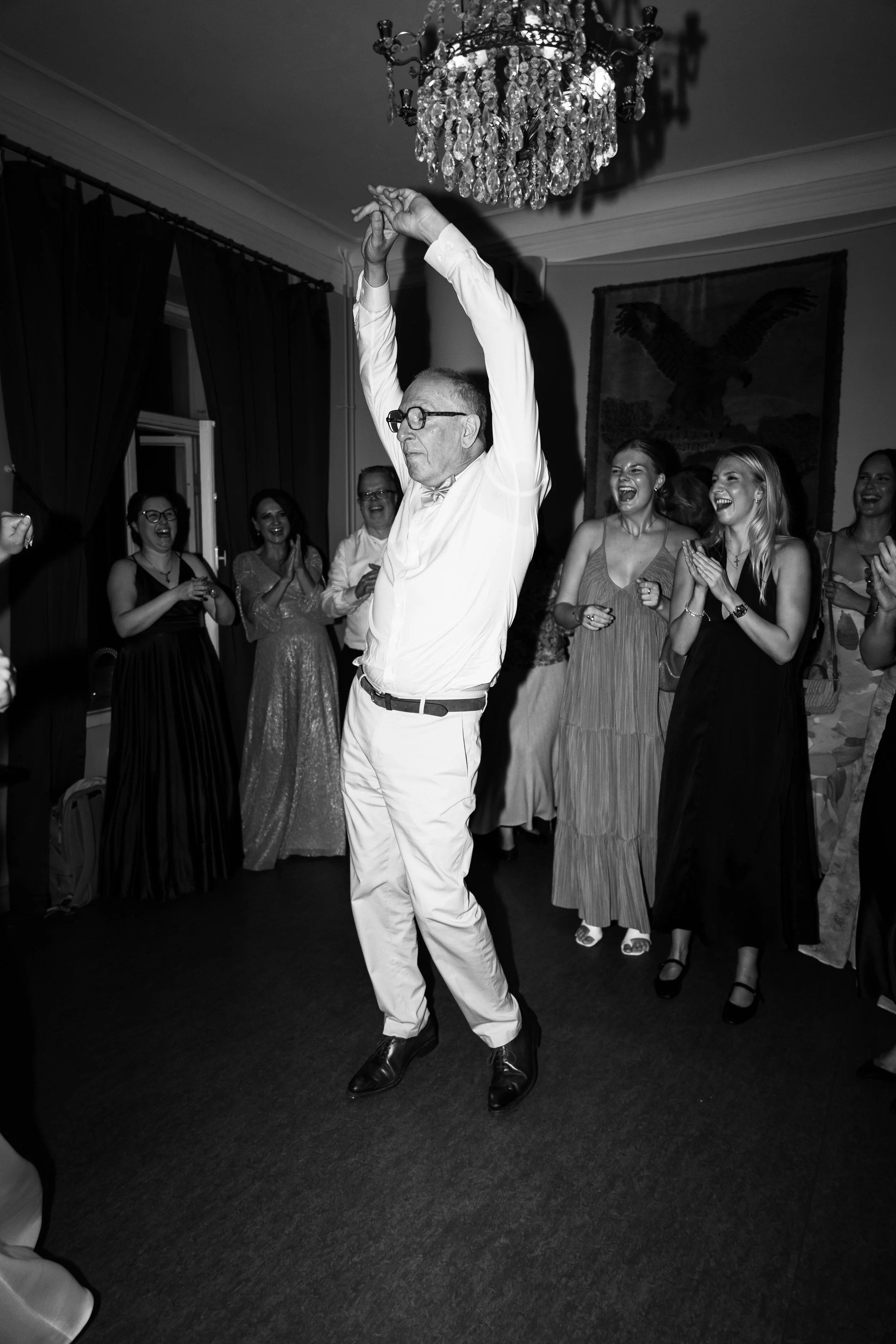 Mies tanssimassa juhlassa, ympärillä nauravia ja iloisia naisia