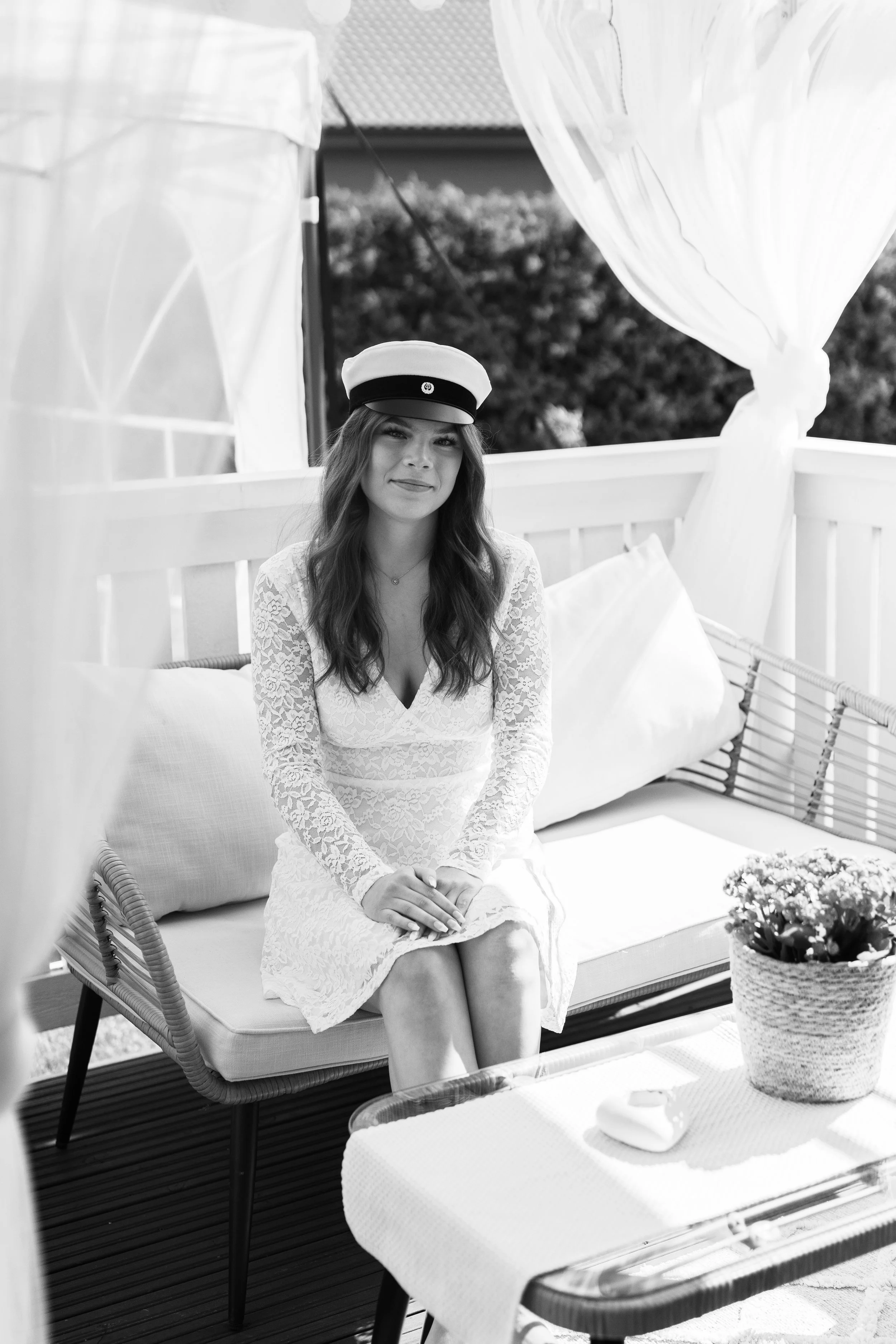 Ylioppilaskuva nuoresta kauniista naisesta. Nainen hymyilee ja istuu oman kotinsa pihalla. On kaunis kesäpäivä.