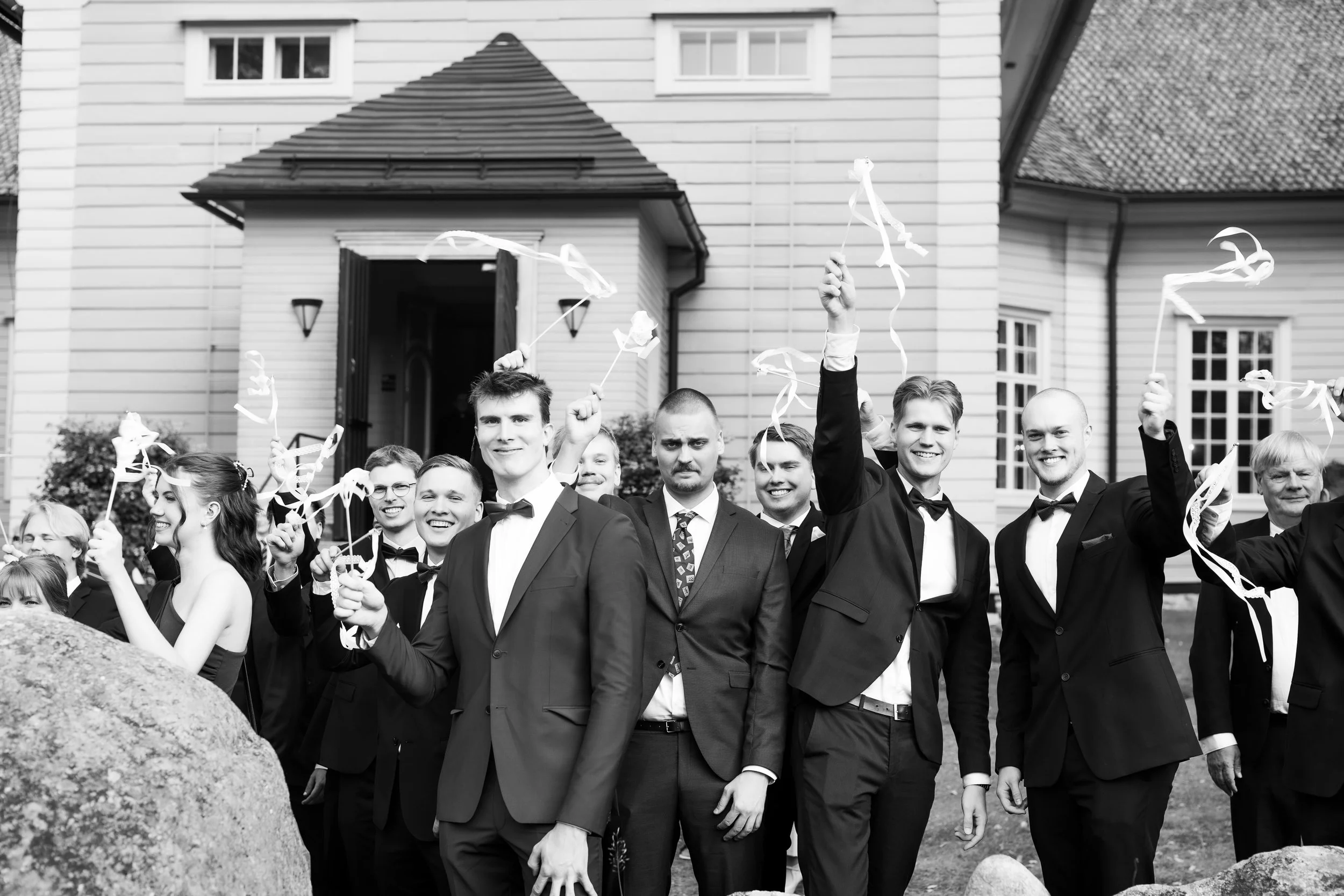 Häiden juhlaväki seisoo porukalla kirkon edessä ja heiluttaa serpenttihuiskuja hääparille. 