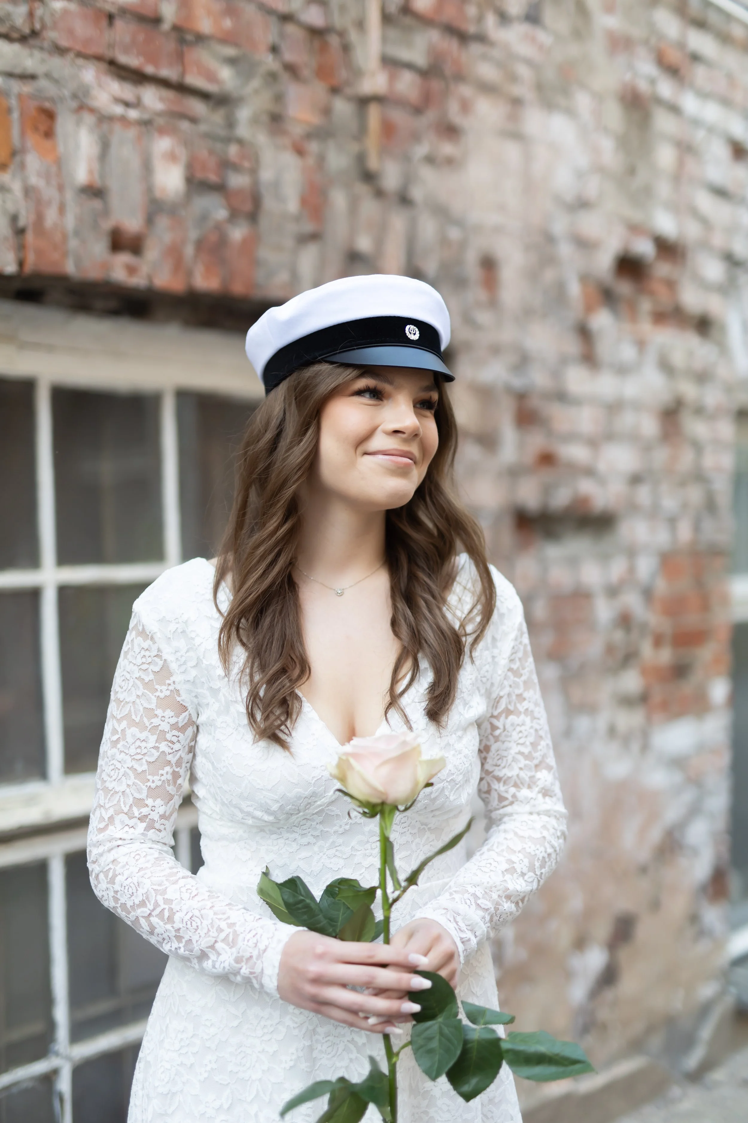 Ylioppilaskuva nuoresta tummatukkaisesta naisesta. Nainen hymyilee ja katsoo poispäin kamerasta. Naisen takana on kaunis tiililato.