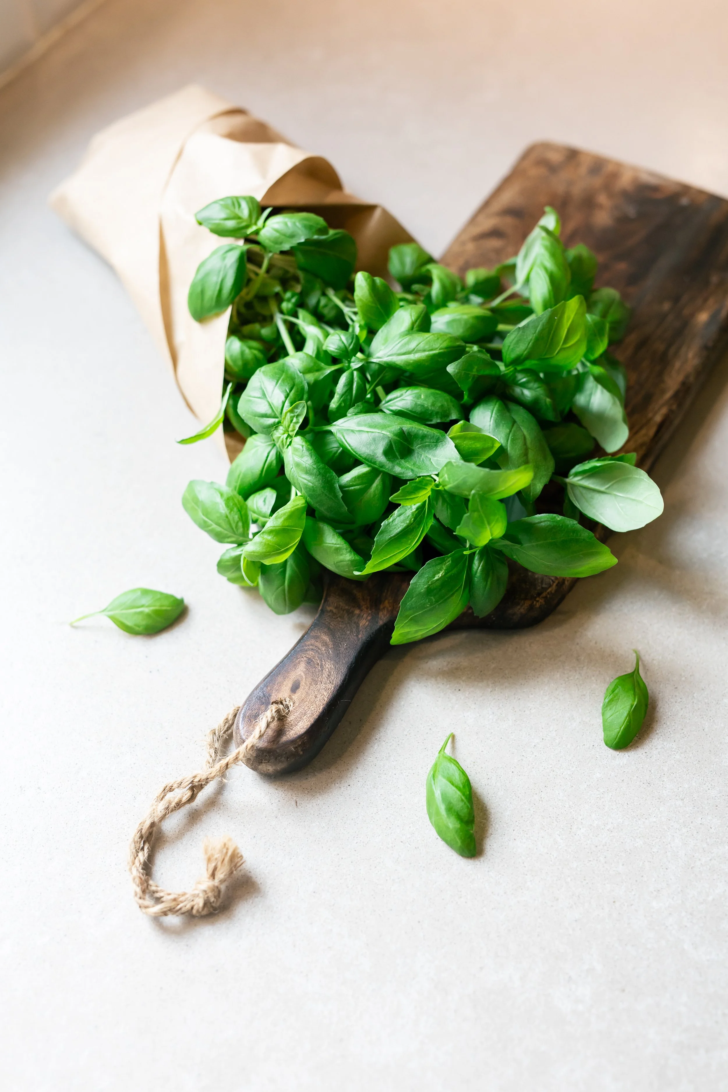Vihreitä basilikan lehtiä puisen leikkuulaudan päällä ja paperipussissa.