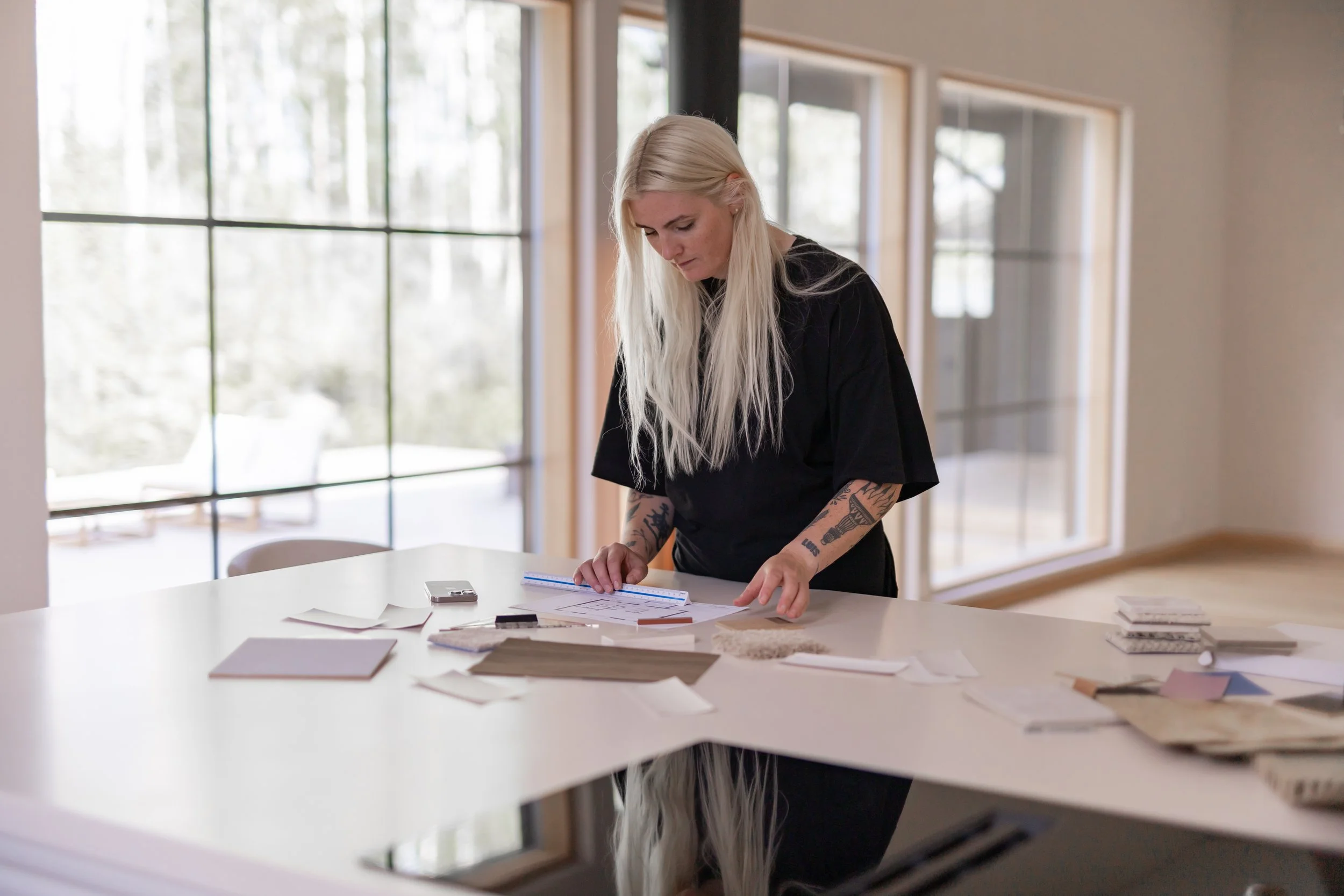 Sisustussuunnittelija suunnittelee kotia asiakkaalleen. Suunnittelija seisoo pöydän ääressä. Hänellä on pitkä vaalea tukka.