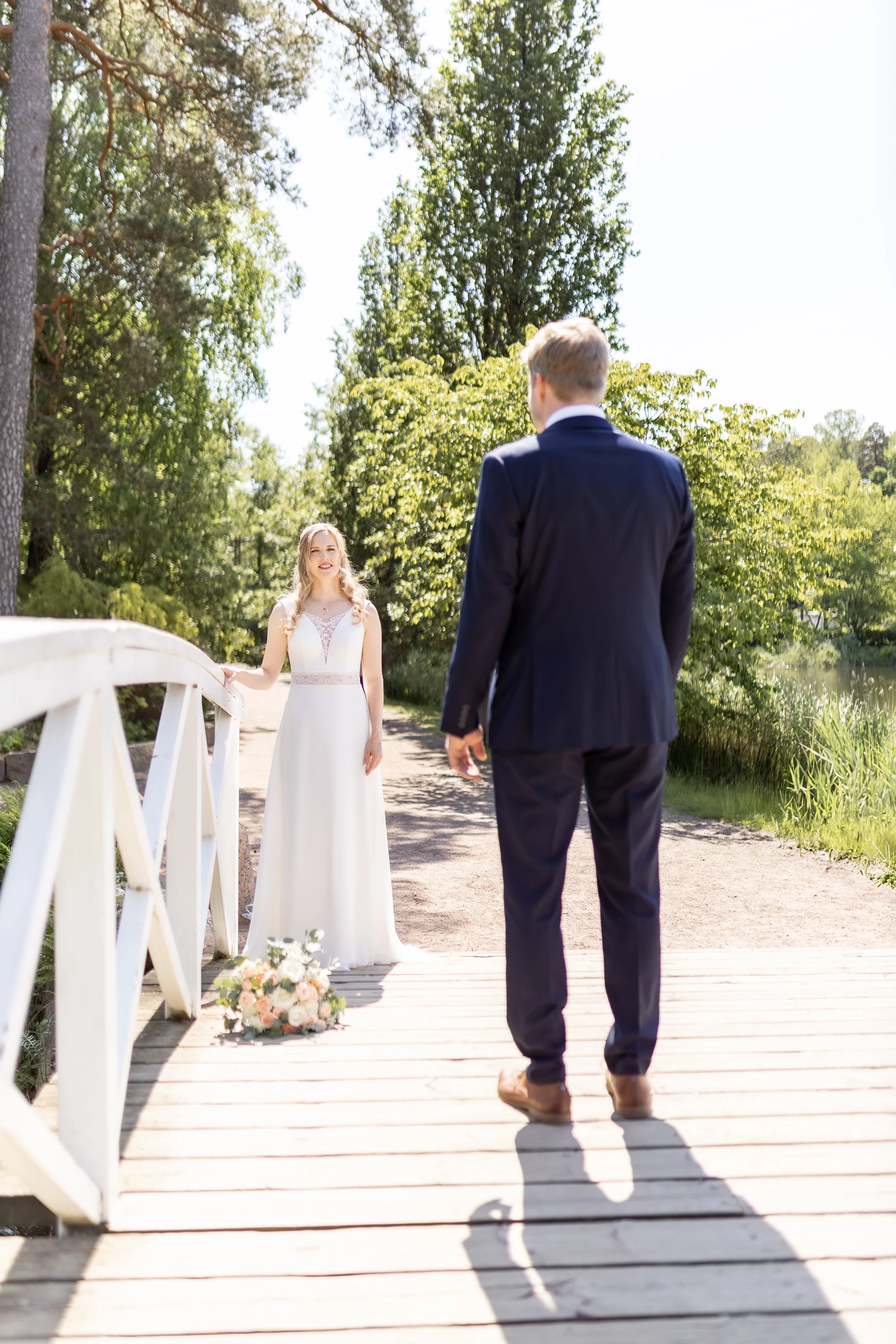 Hääpari asettuu risteyksessä luonnon keskellä, nainen häämekossa ja mies pikkutakissa, valoisassa päivässä, kaunis puistomiljöö.