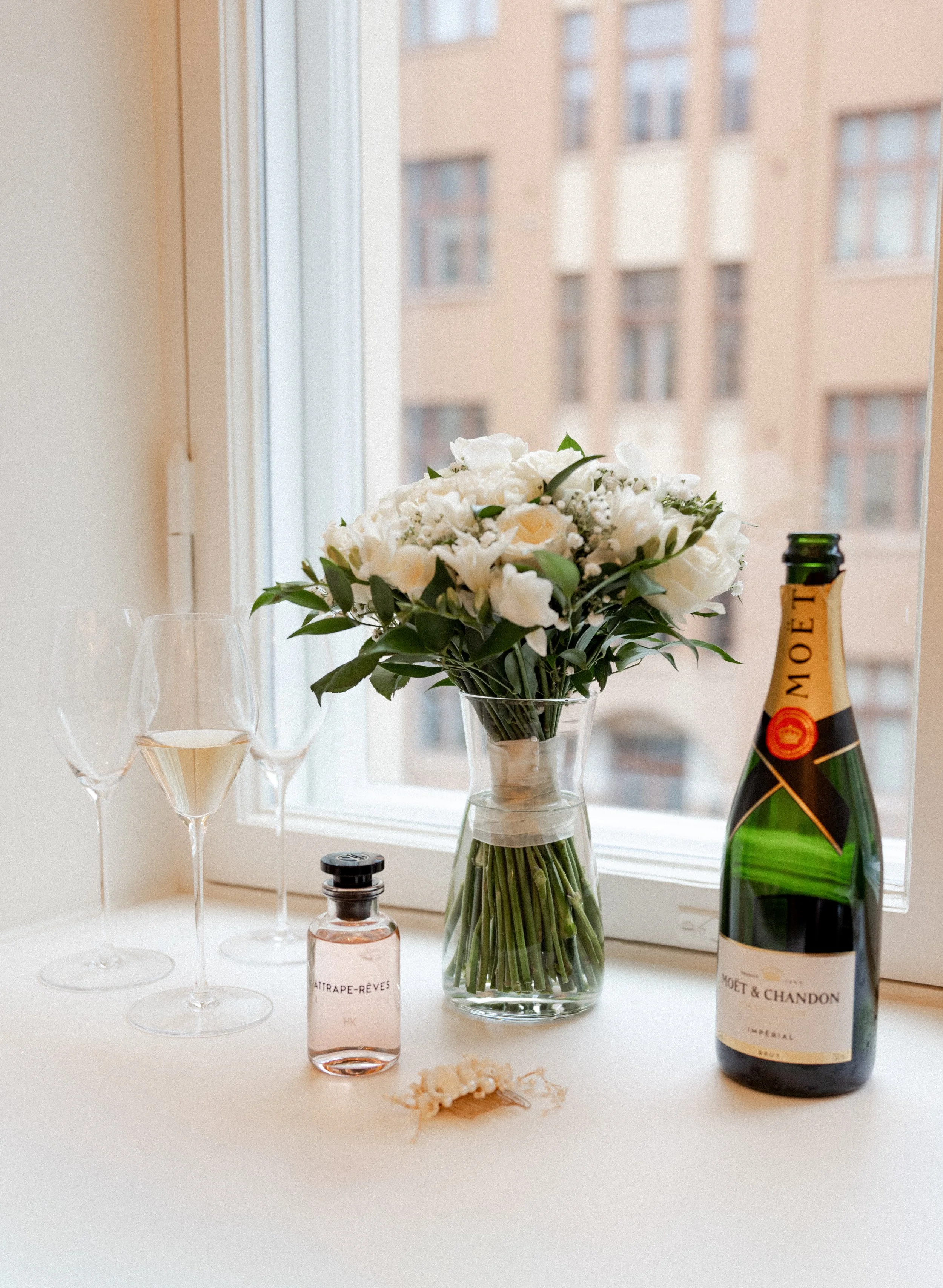 Kukkakimppu, kolme viinilasia, pieni shampanjapullo, vaaleanpunainen hajuvesipulkki ja tilkkuhius