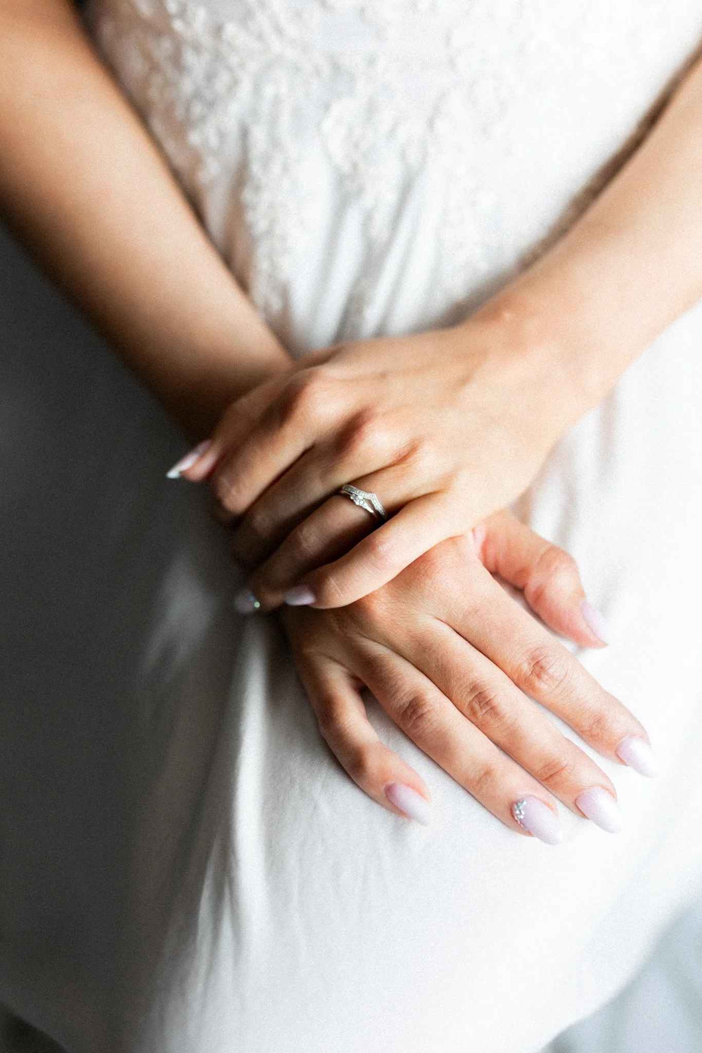 Kuvia morsiamen käsistä. Kuvassa näkyy kauniit vihkisormukset ja hääpuku taustalla.