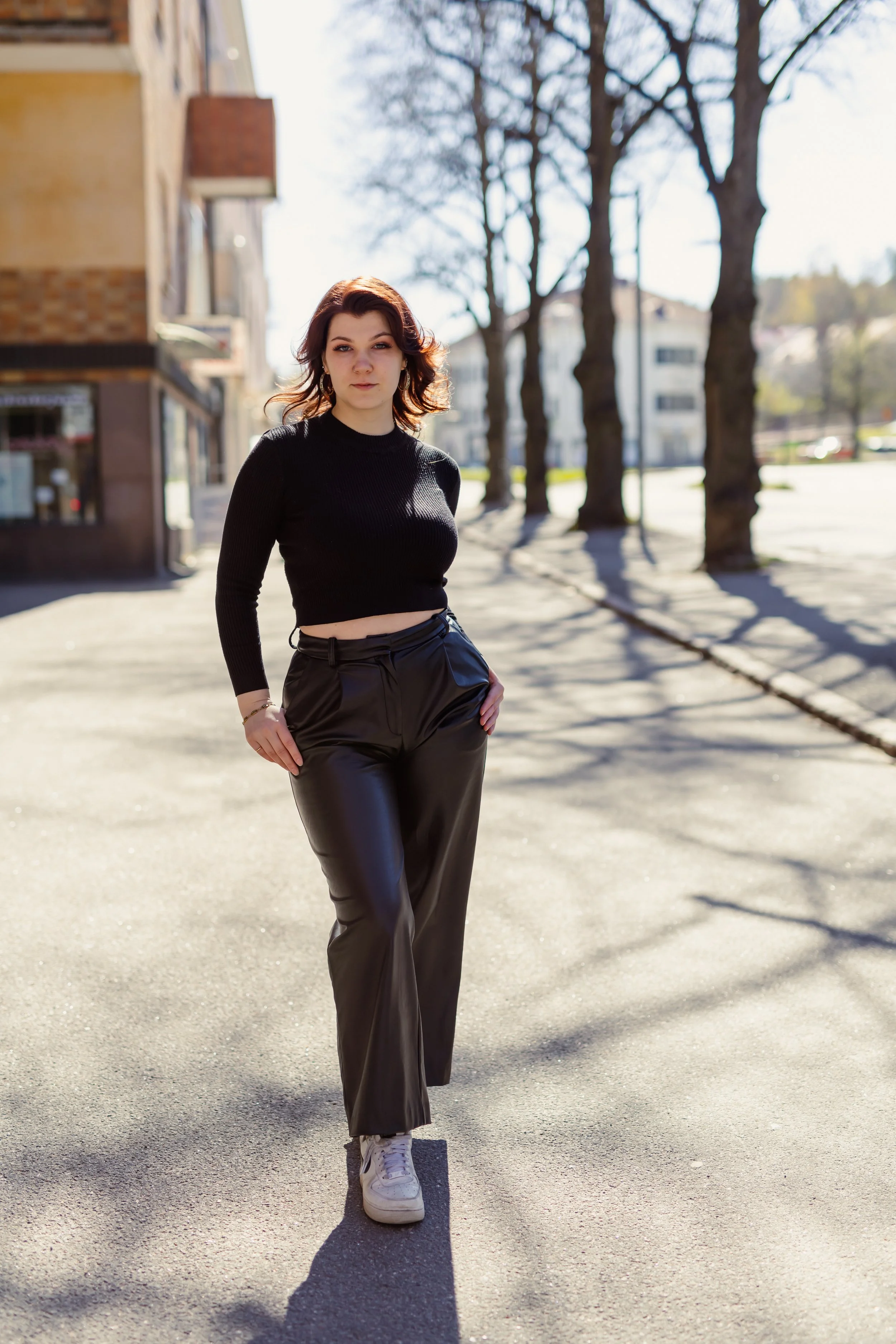 Nuoret nainen kävelee kadulla aurinkoisena päivänä, taustalla puut ja rakennukset.