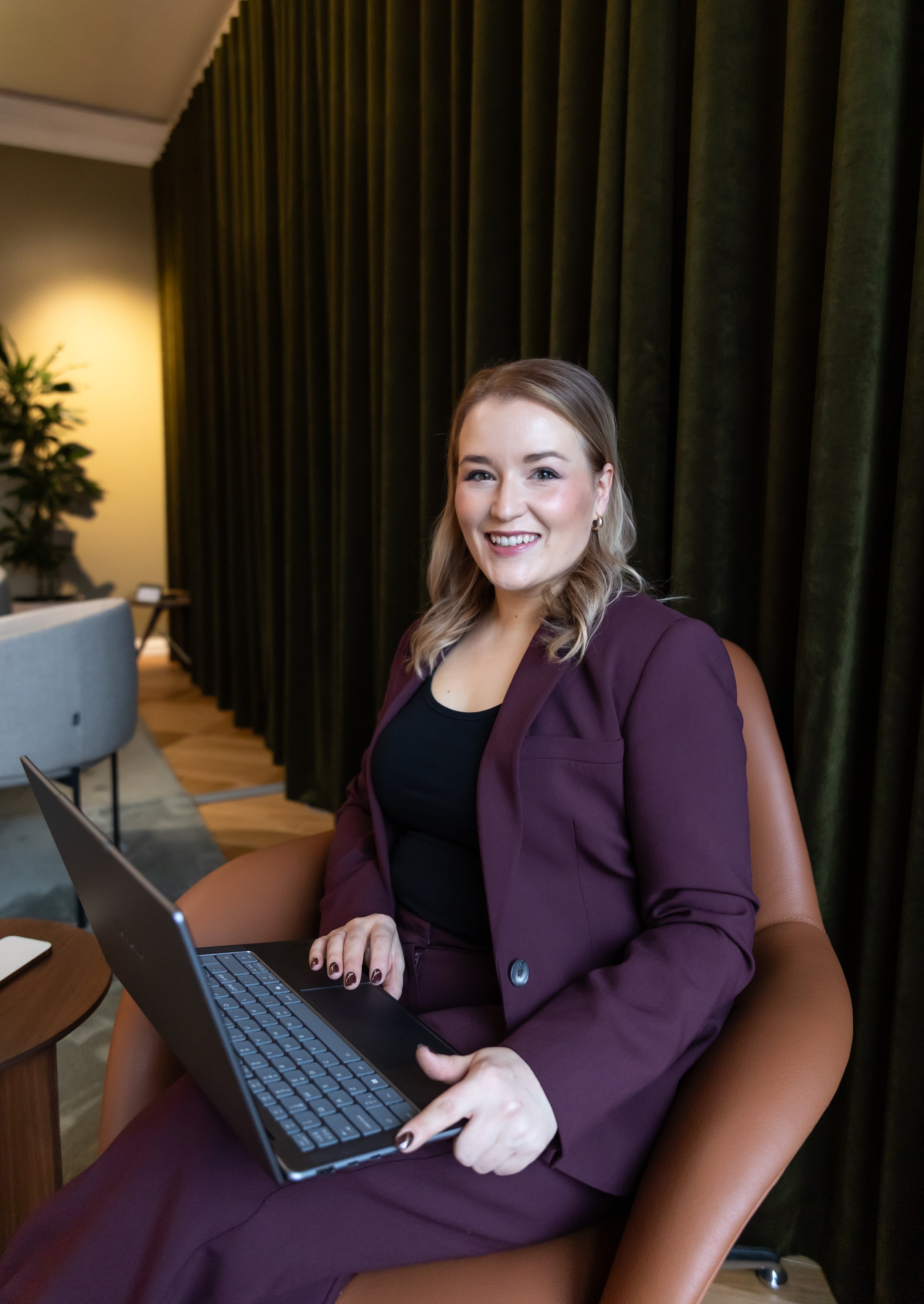 Henkilö naisesta joka istuu nojatuolissa tietokone sylissään. Nainen tekee töitä.