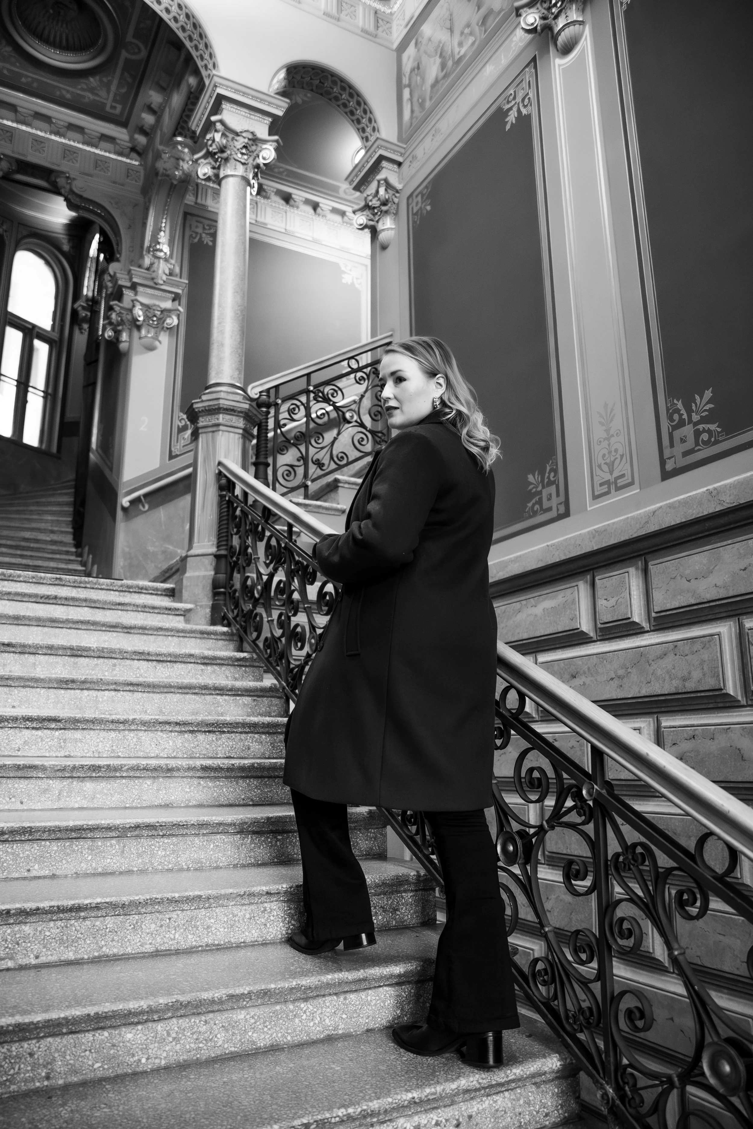 Nainen kävelee portaikkoa ylöspäin ja katsoo sivulle. 