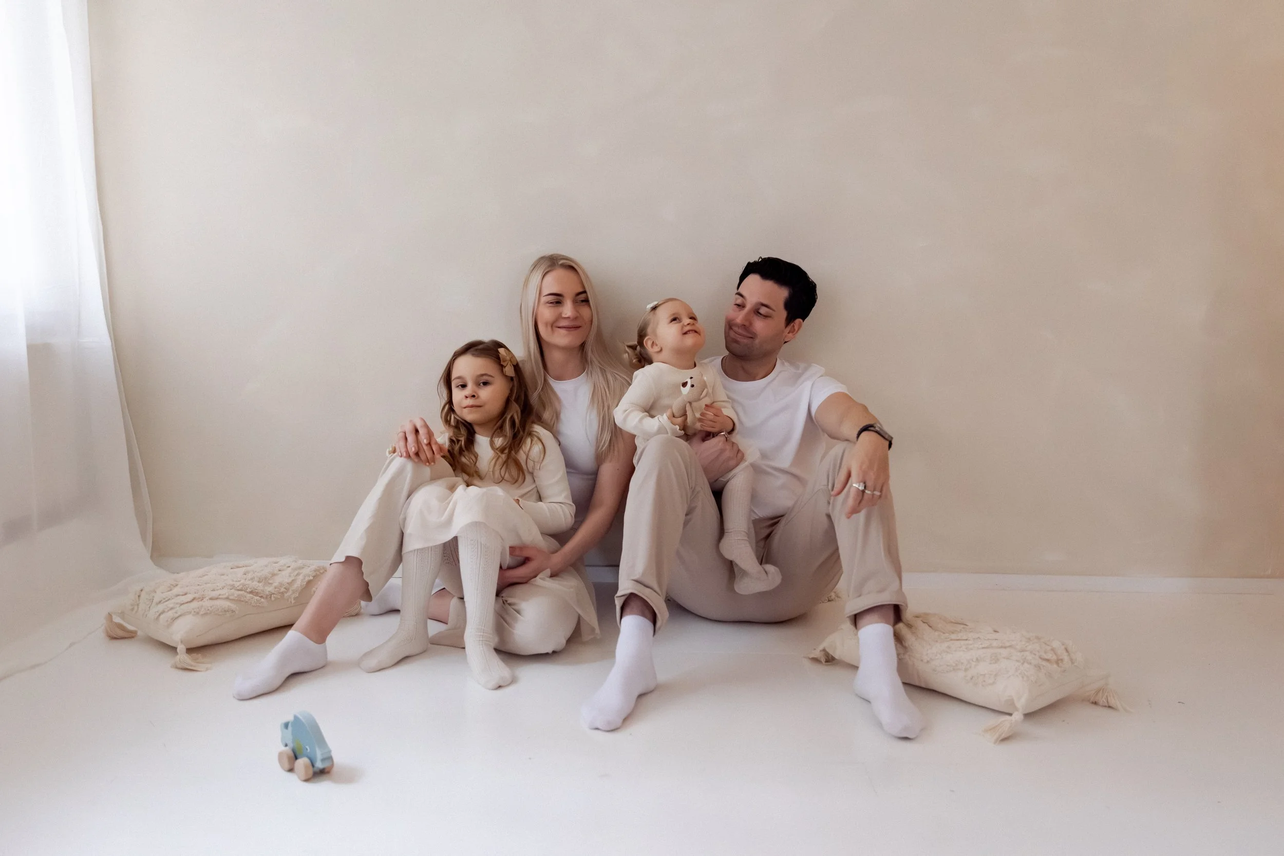 Perhe istuu lattialla ja hassuttelee. Kaunis perhekuva joka on otettu valokuvausstudiossa. 