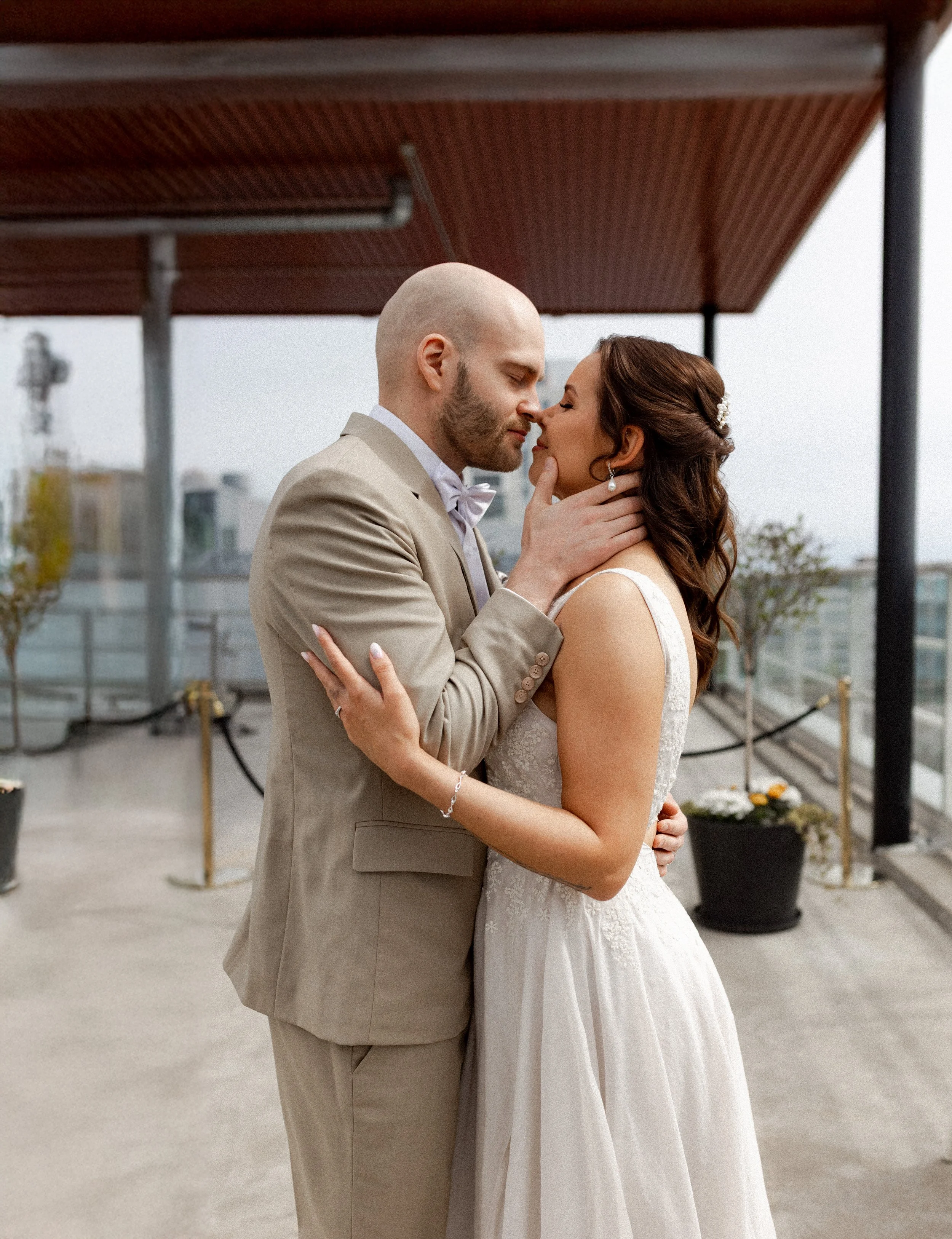Hääpari suutelee toisiaan kauniin hotellin katolla. Morsiamella on kaunis valkoinen hääpuku ja miehellä beige puku.