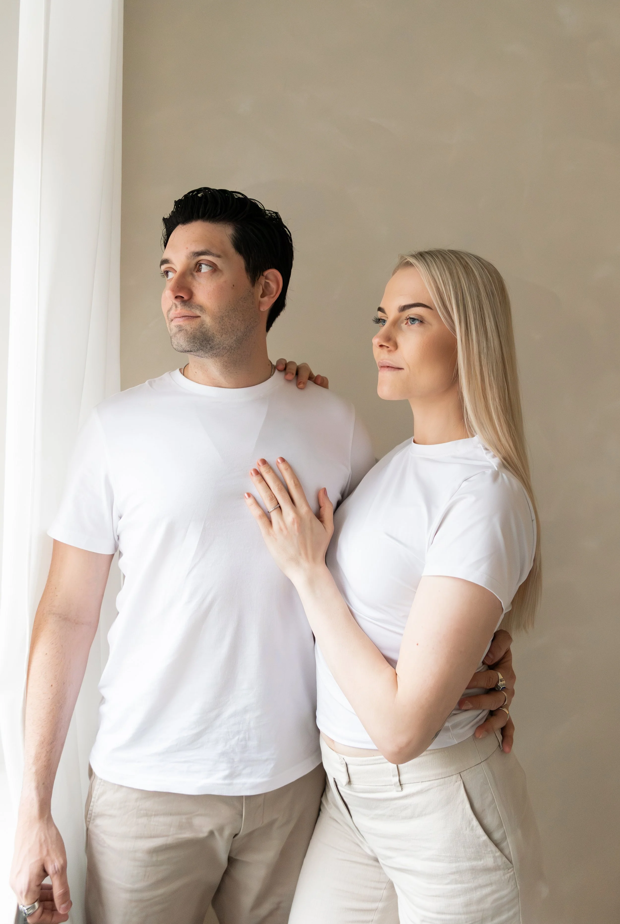 Pariskunta seisoo vierekkäin ja nainen pitää miehestään kiinni. Pariskunta katsoo ulos yhdessä.